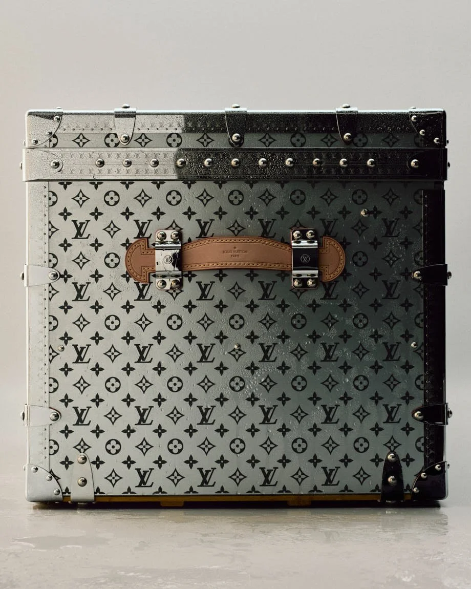 Silver-toned Louis Vuitton Monogram case with a tan leather handle and dark riveted edging.