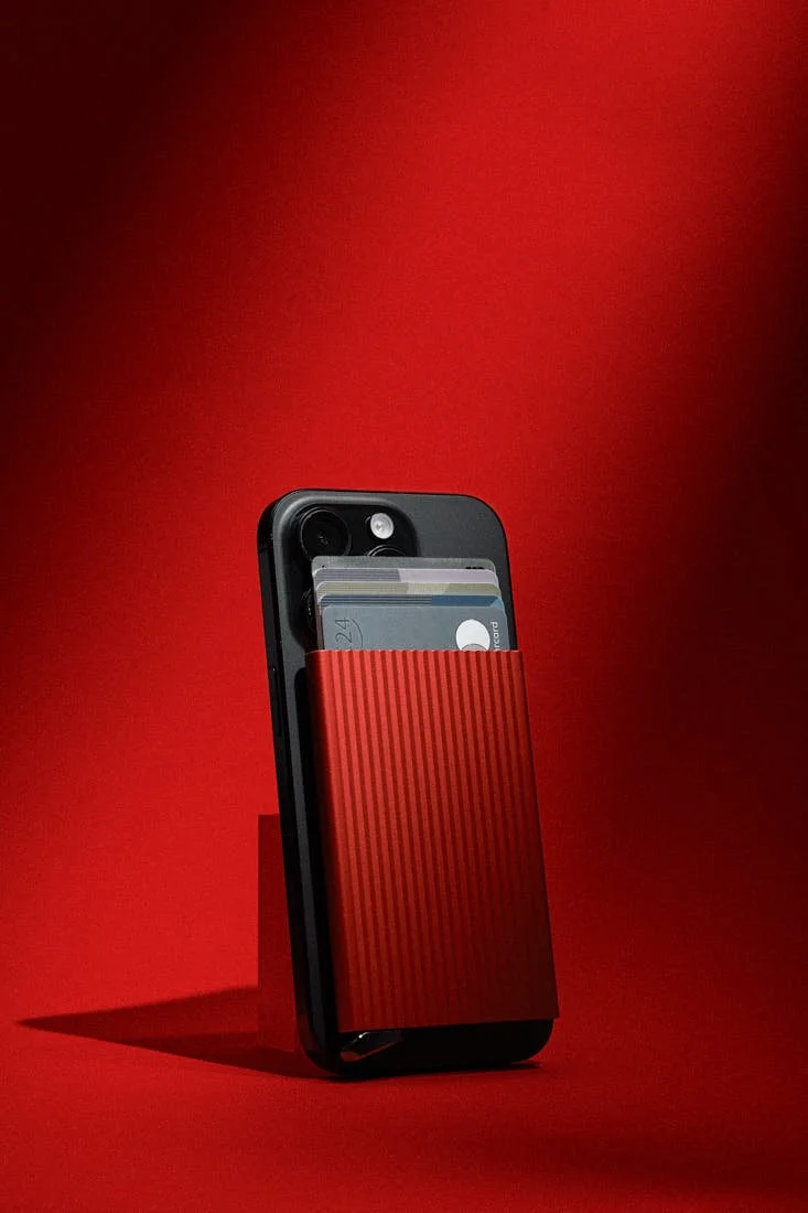 SECRID Premium Cardprotector+ Fluted for MagSafe in red attached to a black smartphone with several cards visible above the fluted aluminium case, photographed against a red background for LE MILE Magazine.