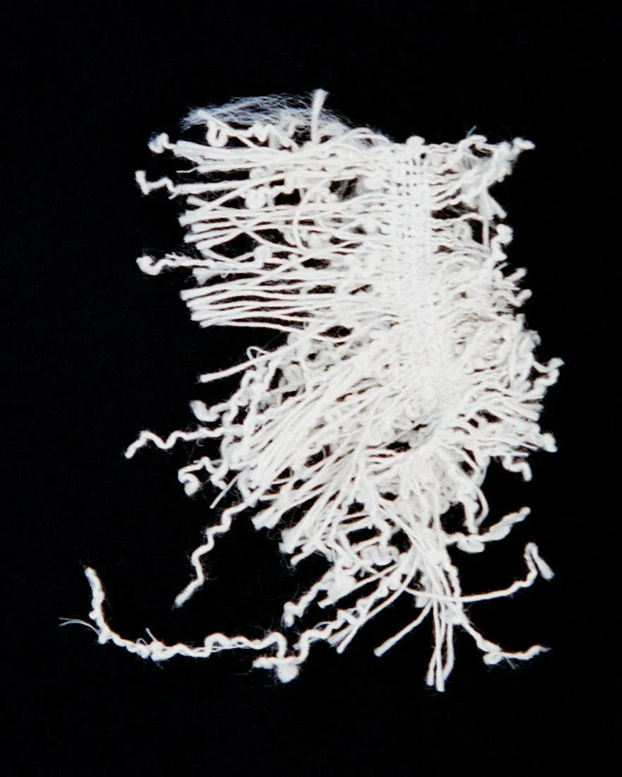 Frayed white textile sample from the Dior Men Summer 2027 collection shown against a black background and held across a hand.