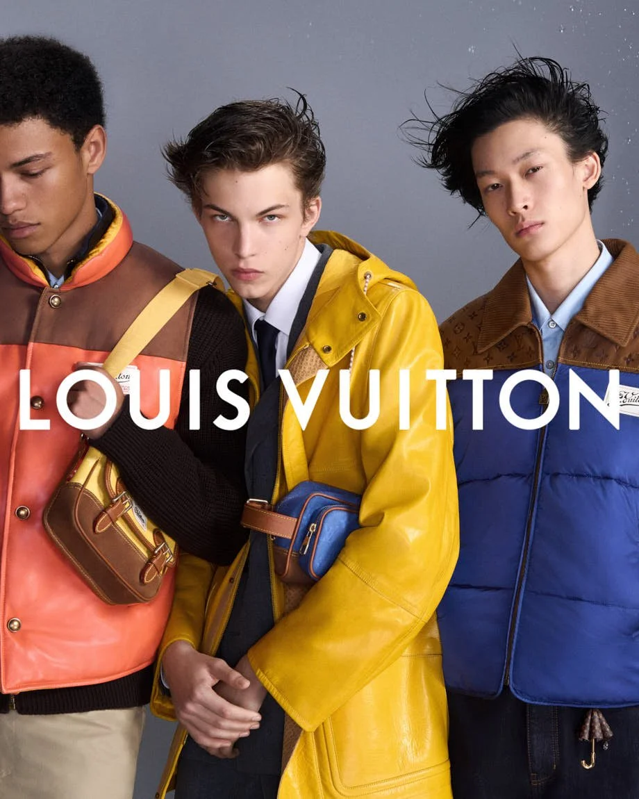 Three models in orange, yellow and blue Louis Vuitton outerwear against a grey backdrop.