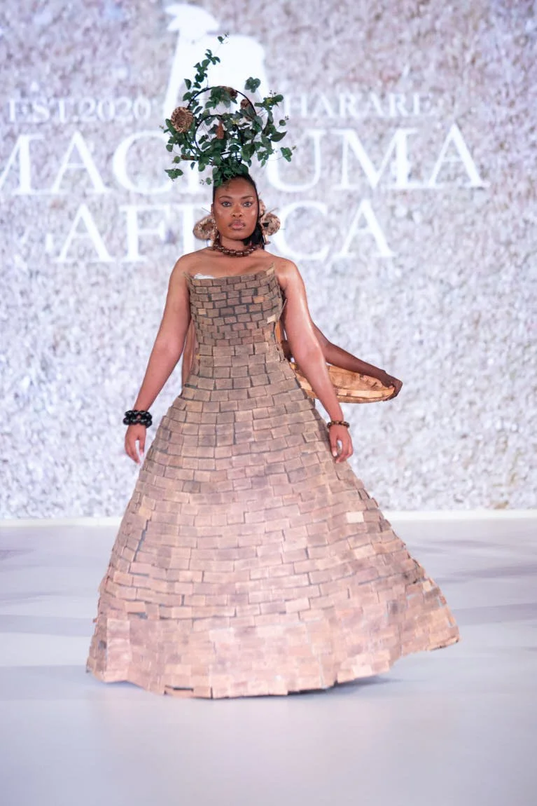 Model presenting a sculptural, floor-length beige gown with a floral headpiece on the runway.
