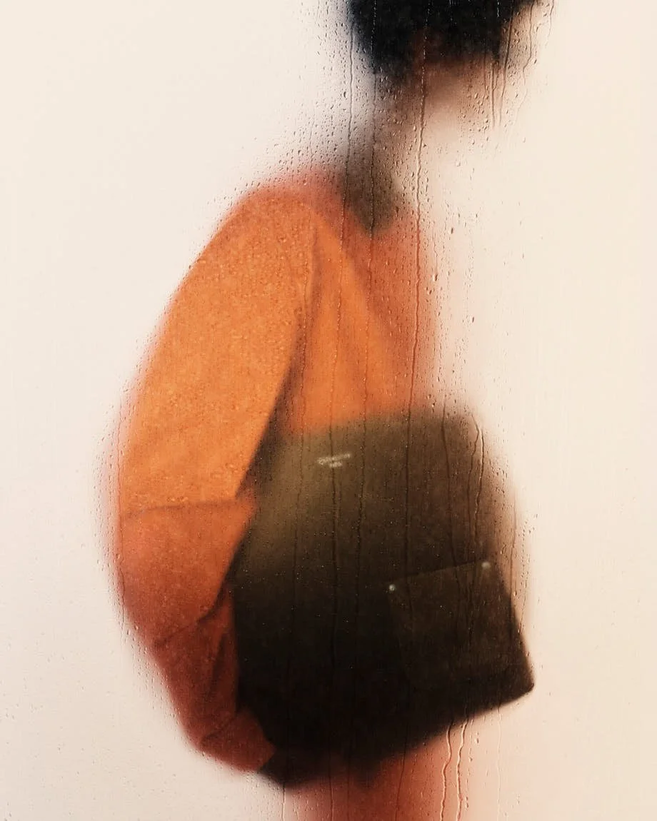Orange Louis Vuitton workwear jacket and a dark brown tote photographed through rain-streaked glass.