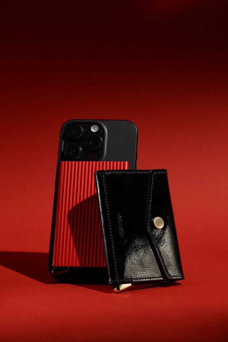 SECRID Premium Cardprotector+ Fluted for MagSafe in red attached to a smartphone alongside the Premium Envelope Wallet+ Naplak in black with glossy leather and gold-tone detail, LE MILE Magazine.