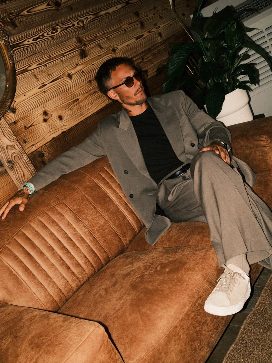 KAAZE seated in a grey suit and sunglasses against a warm wood interior — LE MILE