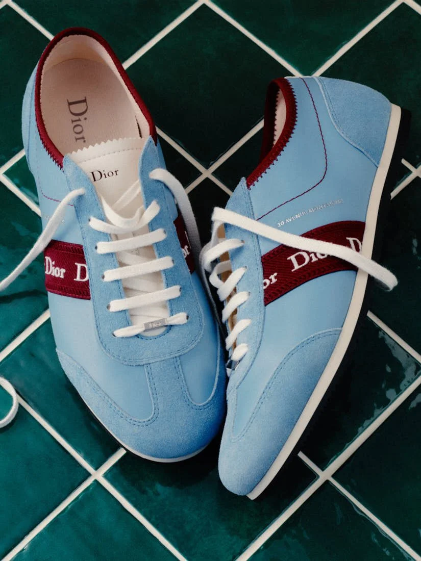 Pale blue Dior Ribbon sneakers with burgundy bands beneath loose blue jeans.