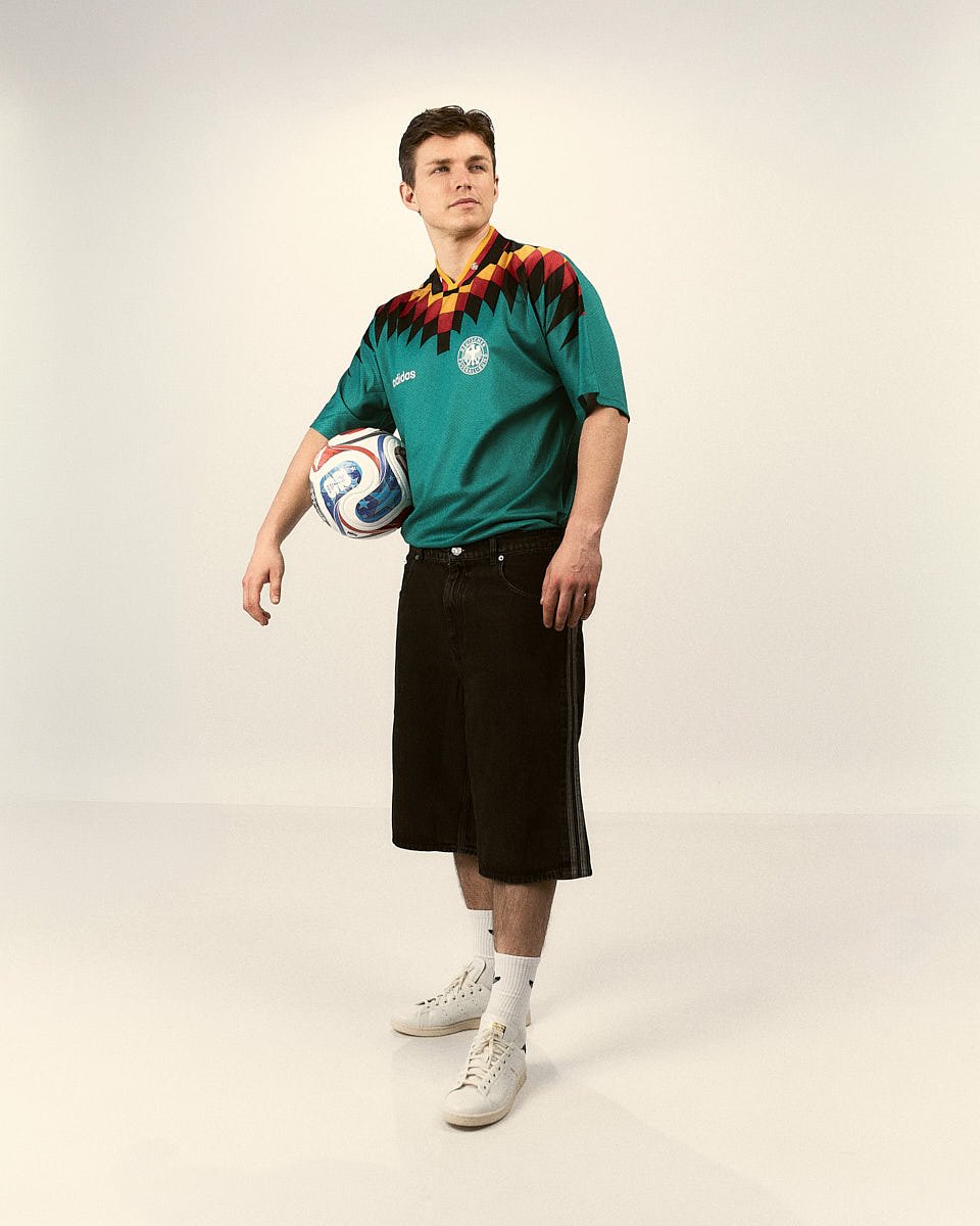 A footballer wears an adidas Originals Germany EQT shirt with black shorts and holds a football in a studio portrait