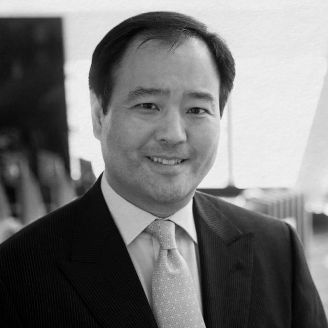 A black and white portrait of an asian man in a suit and tie, smiling at the camera.