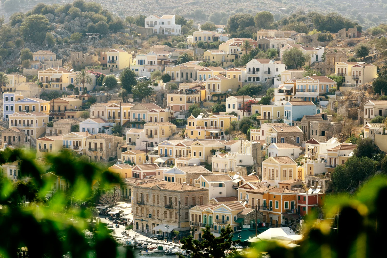 Paisagem de uma vila com casas coloridas na encosta de uma colina, com vegetação e mar no primeiro plano.