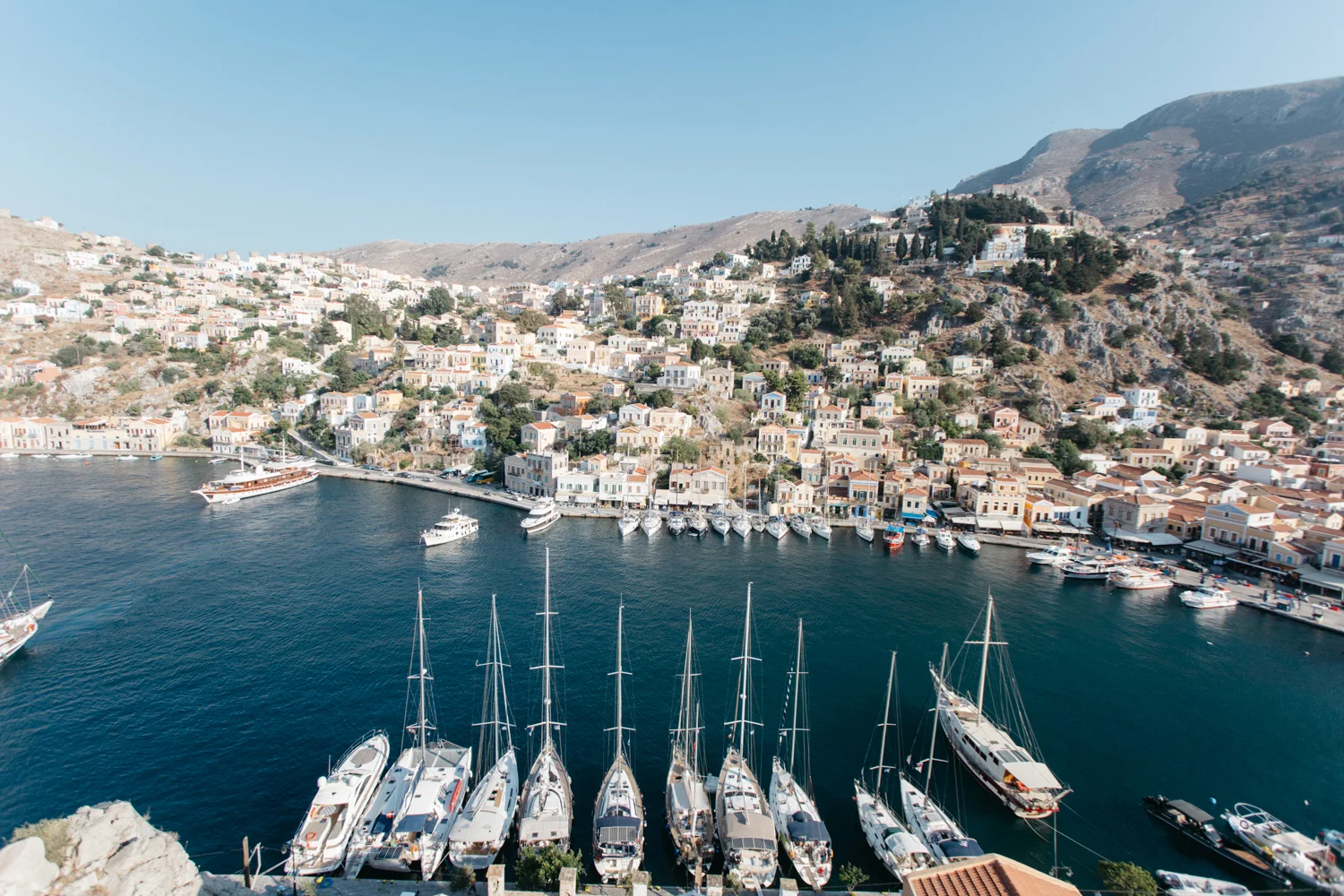 Vista do mar com iates e barcos ancorados, e colinas com casas em estilo mediterrâneo