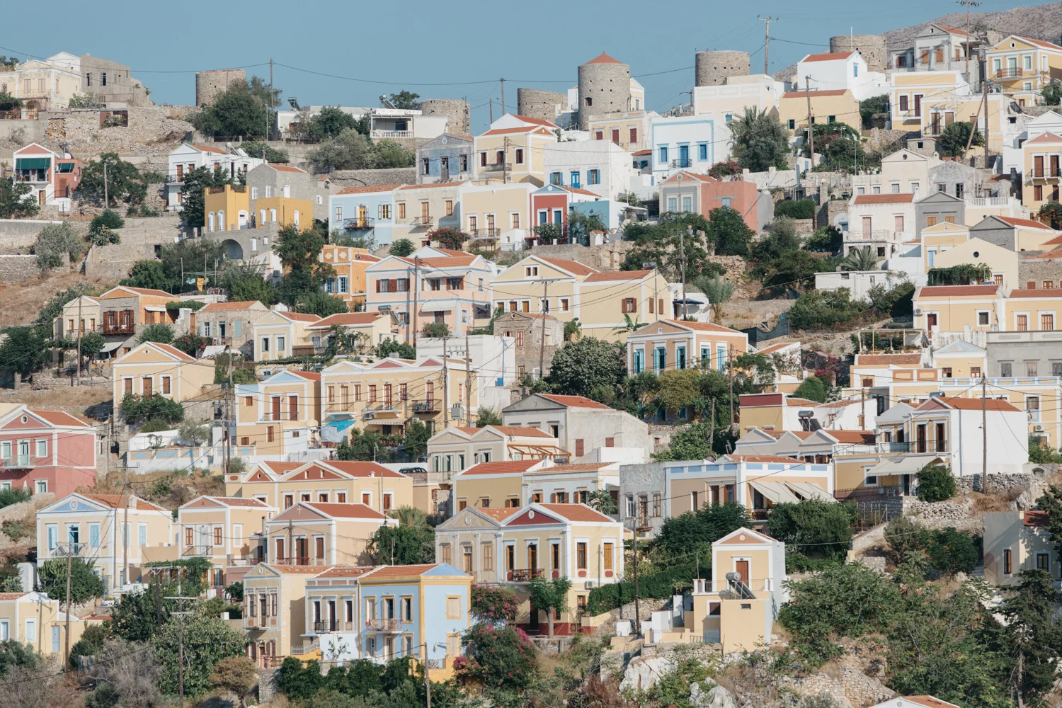 Paisagem de uma cidade costeira com casas coloridas em uma encosta, com colinas ao fundo.