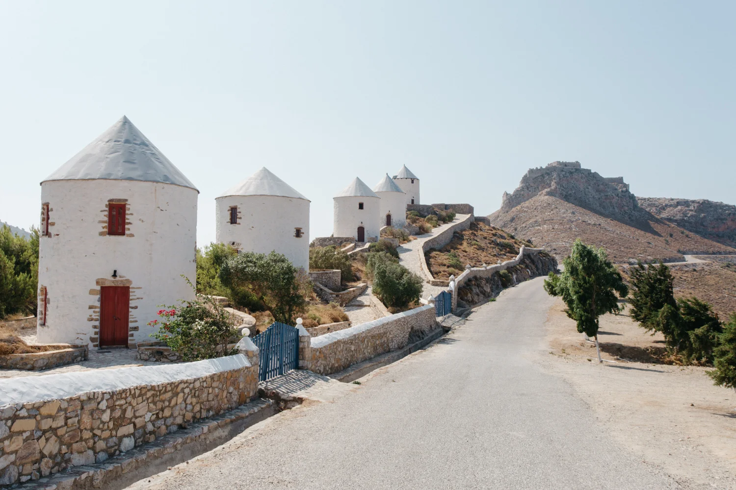 Caminho com casas de pedra e telhados brancos em uma paisagem desértica, com montanhas no fundo.