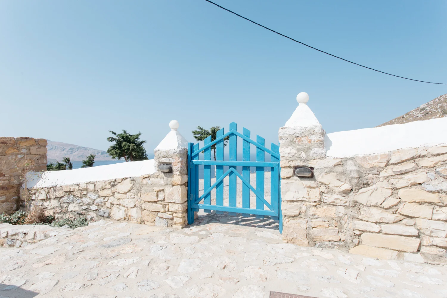 Portão azul de madeira entre muros de pedra, com céu claro ao fundo