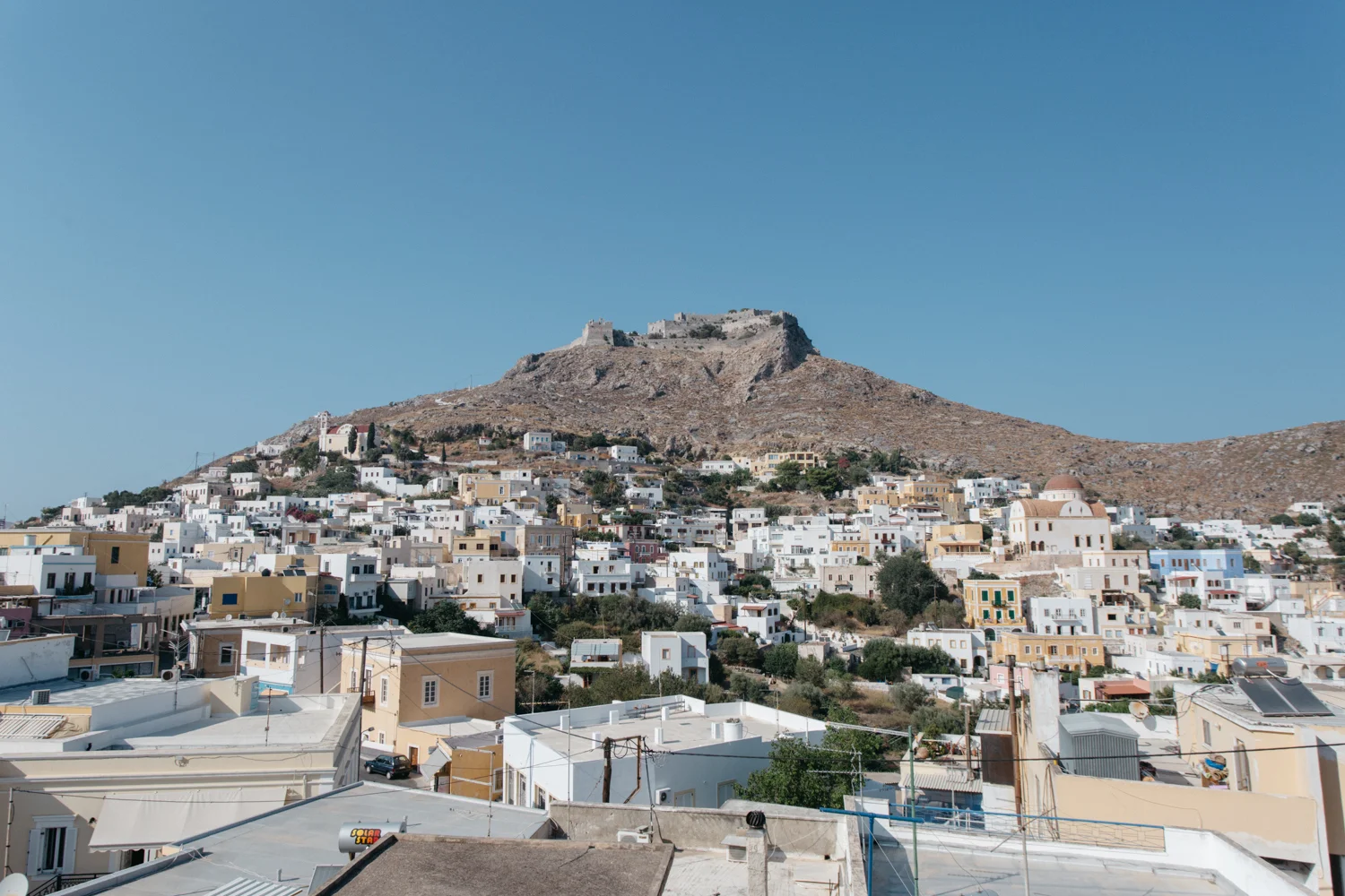 Paisagem de uma cidade com casas brancas e um castelo no topo de uma colina rochosa sob céu claro.