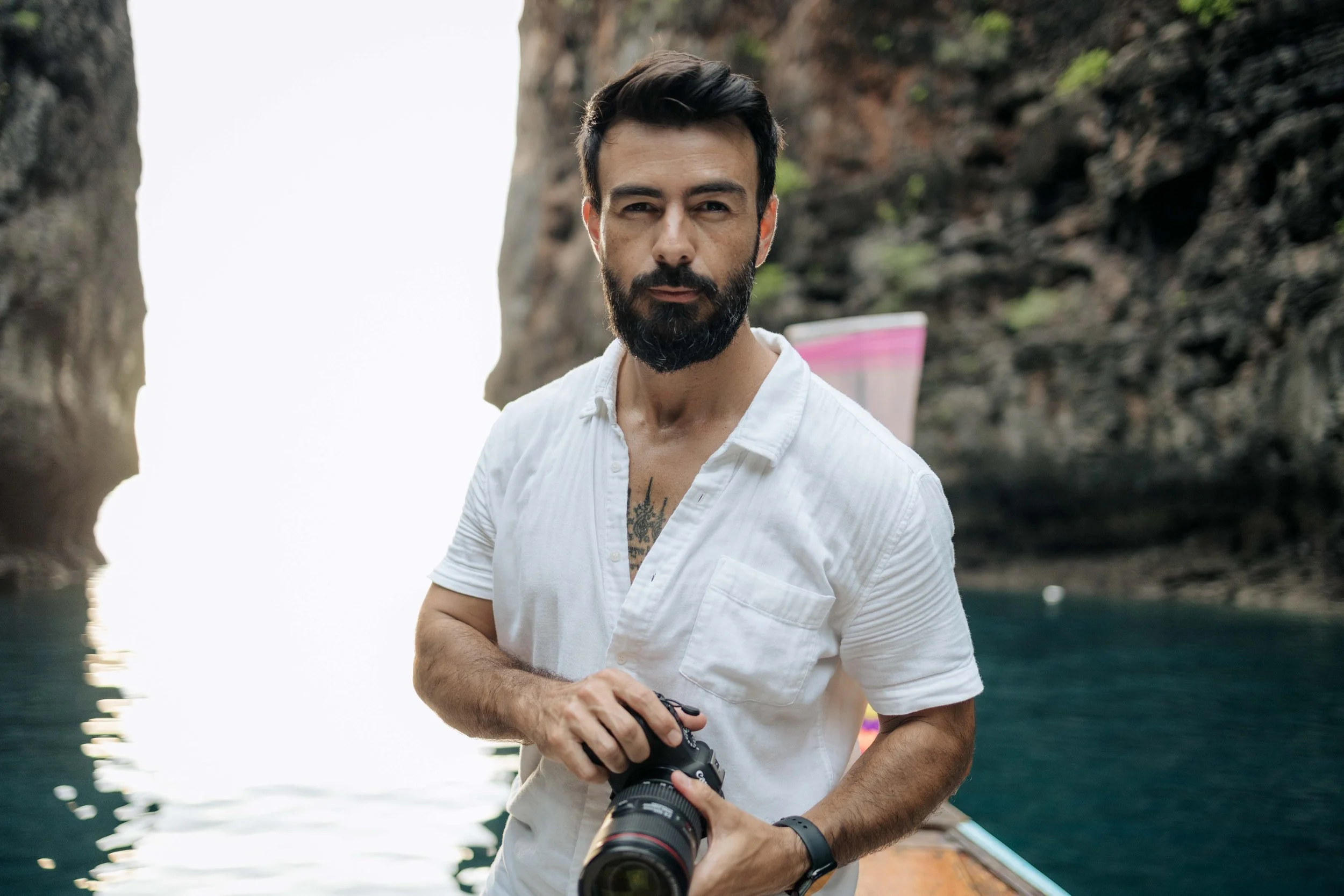 Um homem barbudo, de camisa branca, está em águas pouco profundas, olhando para o horizonte.
