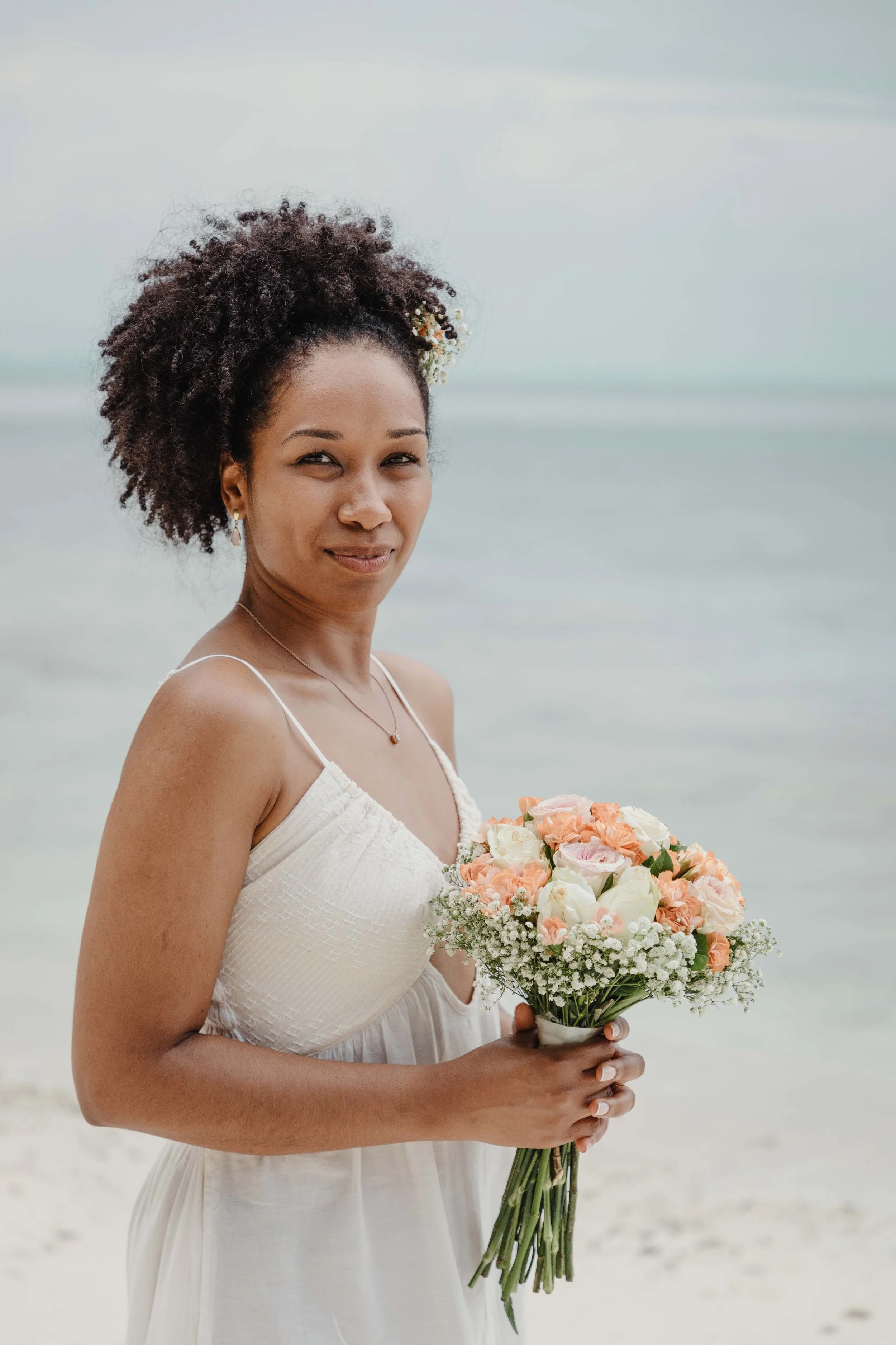 Uma mulher de cabelo encaracolado sorri enquanto segura um vibrante ramo de flores nas mãos.