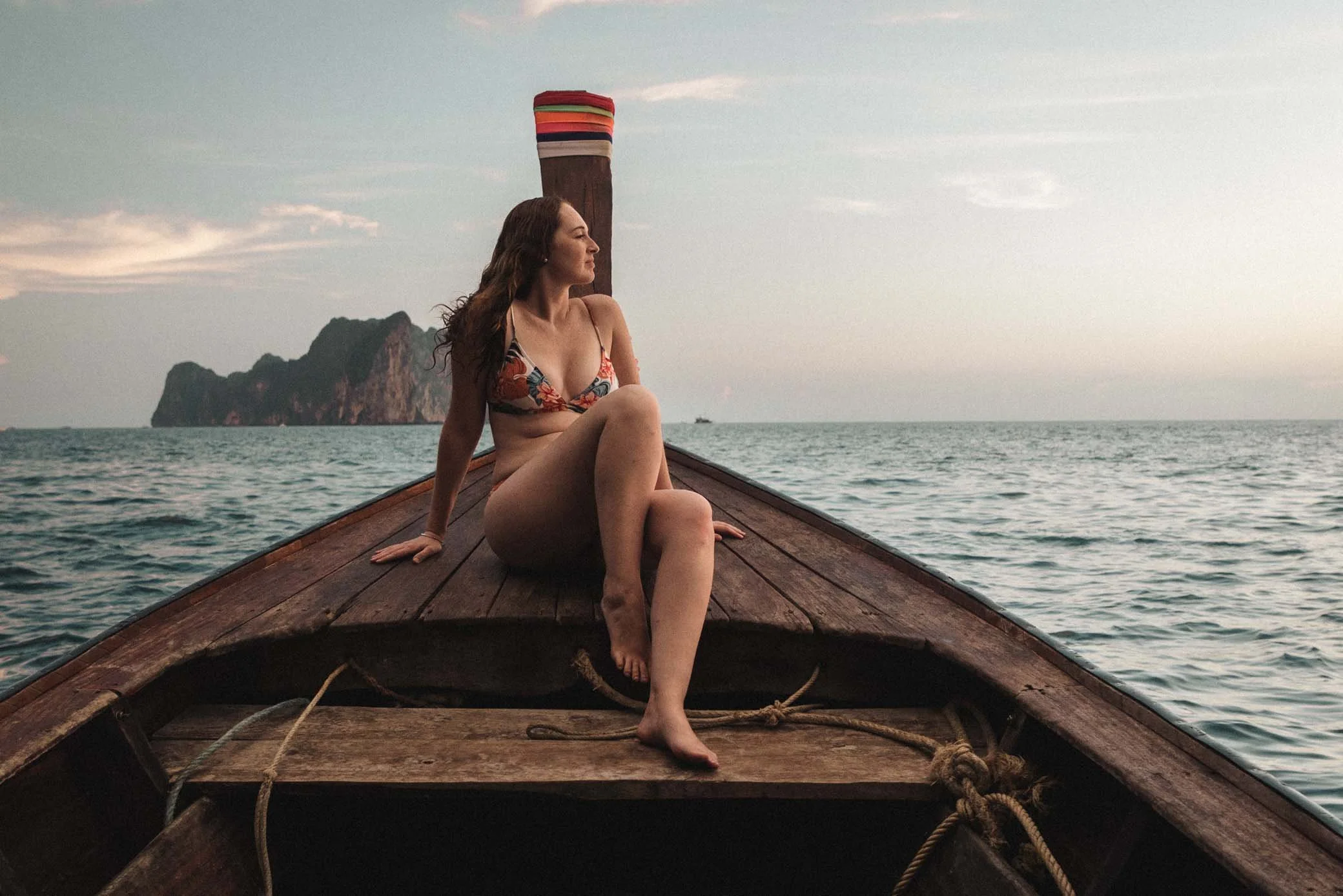 Uma mulher em biquíni relaxa na popa de um barco, aproveitando o sol e a vista para o mar.