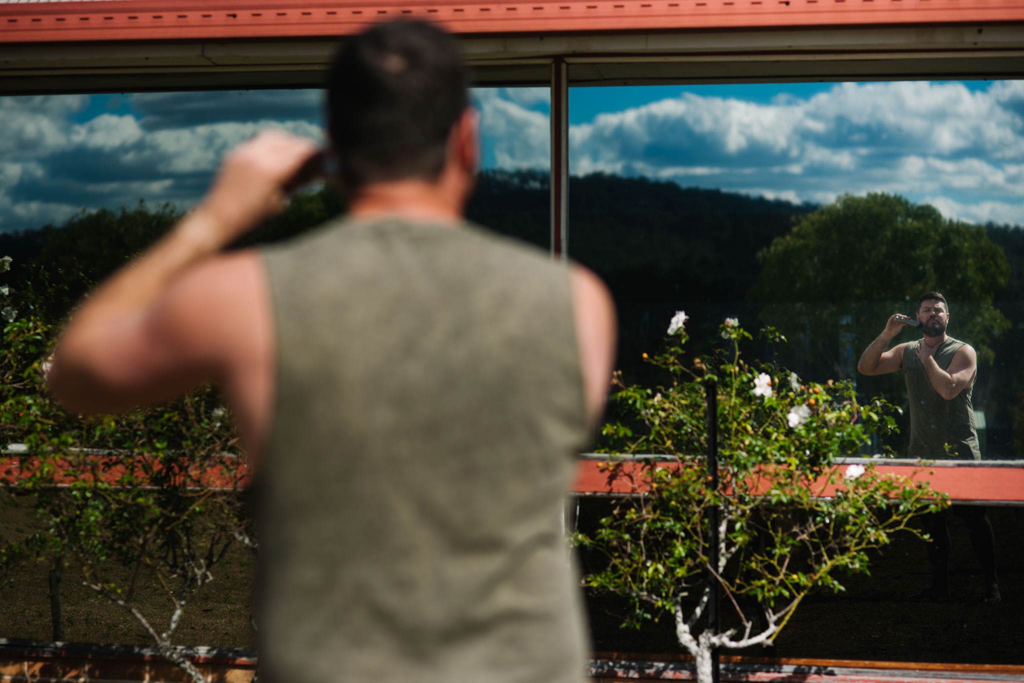 Groom shaving outside using window as a mirror