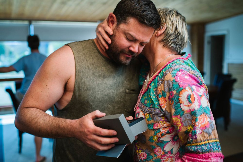 Groom and mother hug as groom opens gift from bride