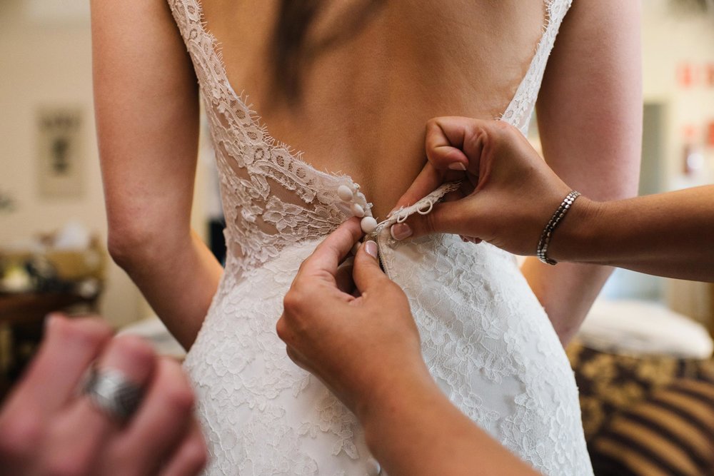 Bridesmaids helping bride button up her dress