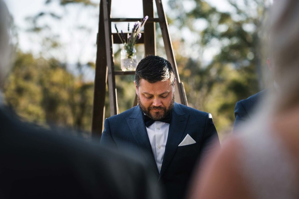 Emotional groom looks down as bride and father walk down aisle