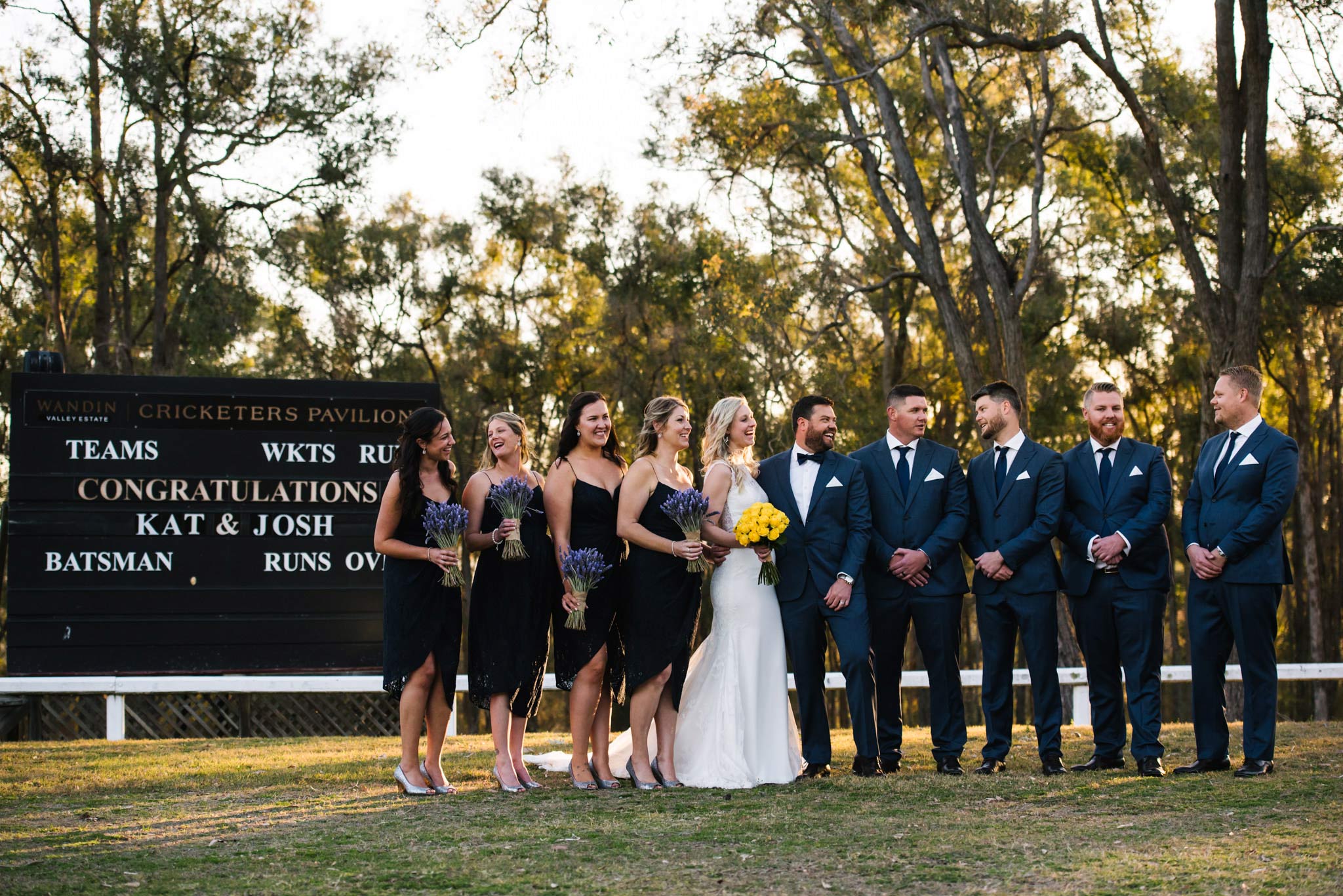 Bridal party in field at Wandin Valley Estate wedding with cricket score board in background