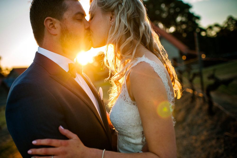 Bride and groom kissing with sun setting in the background