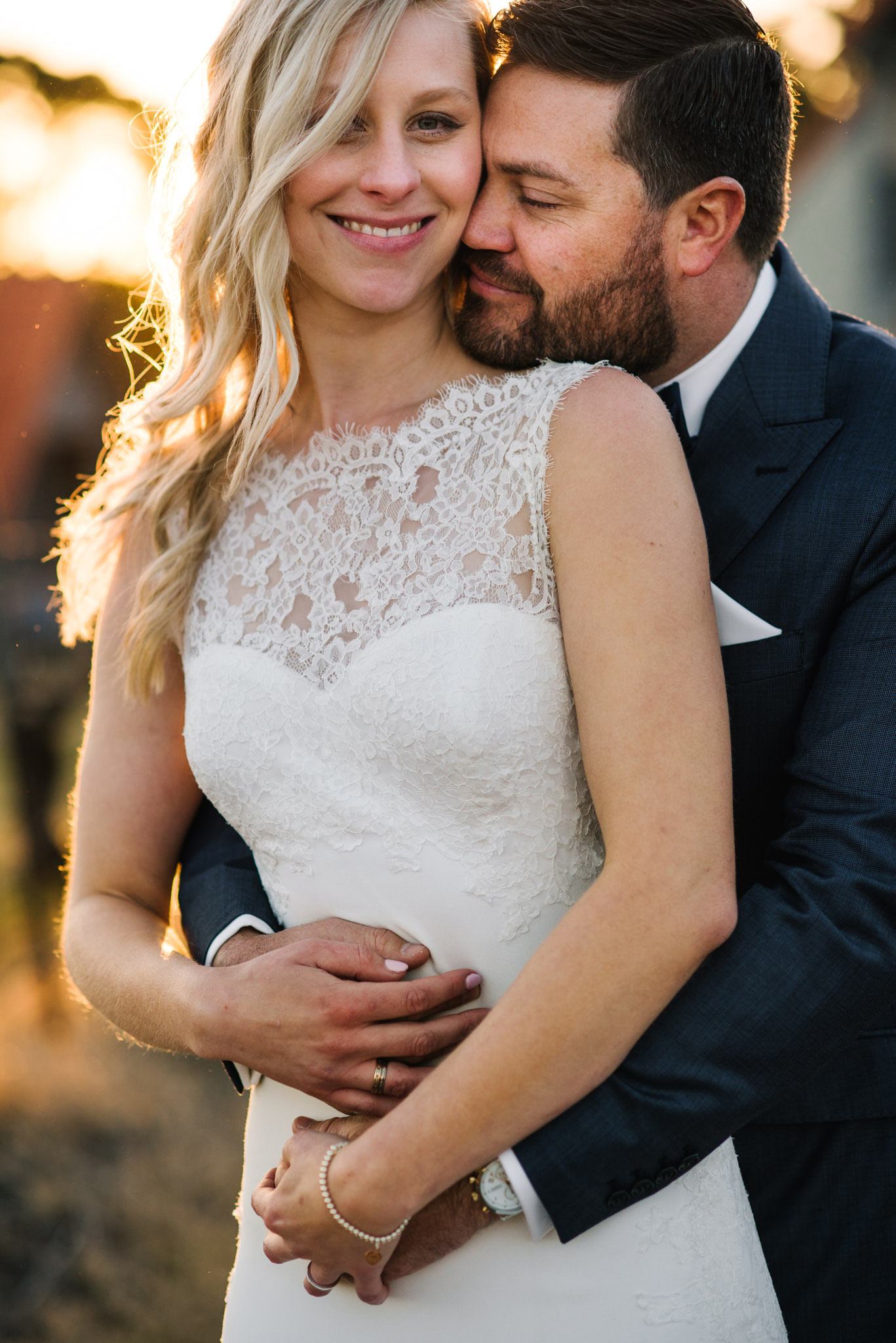 Bride and groom embrace with bride smiling at camera