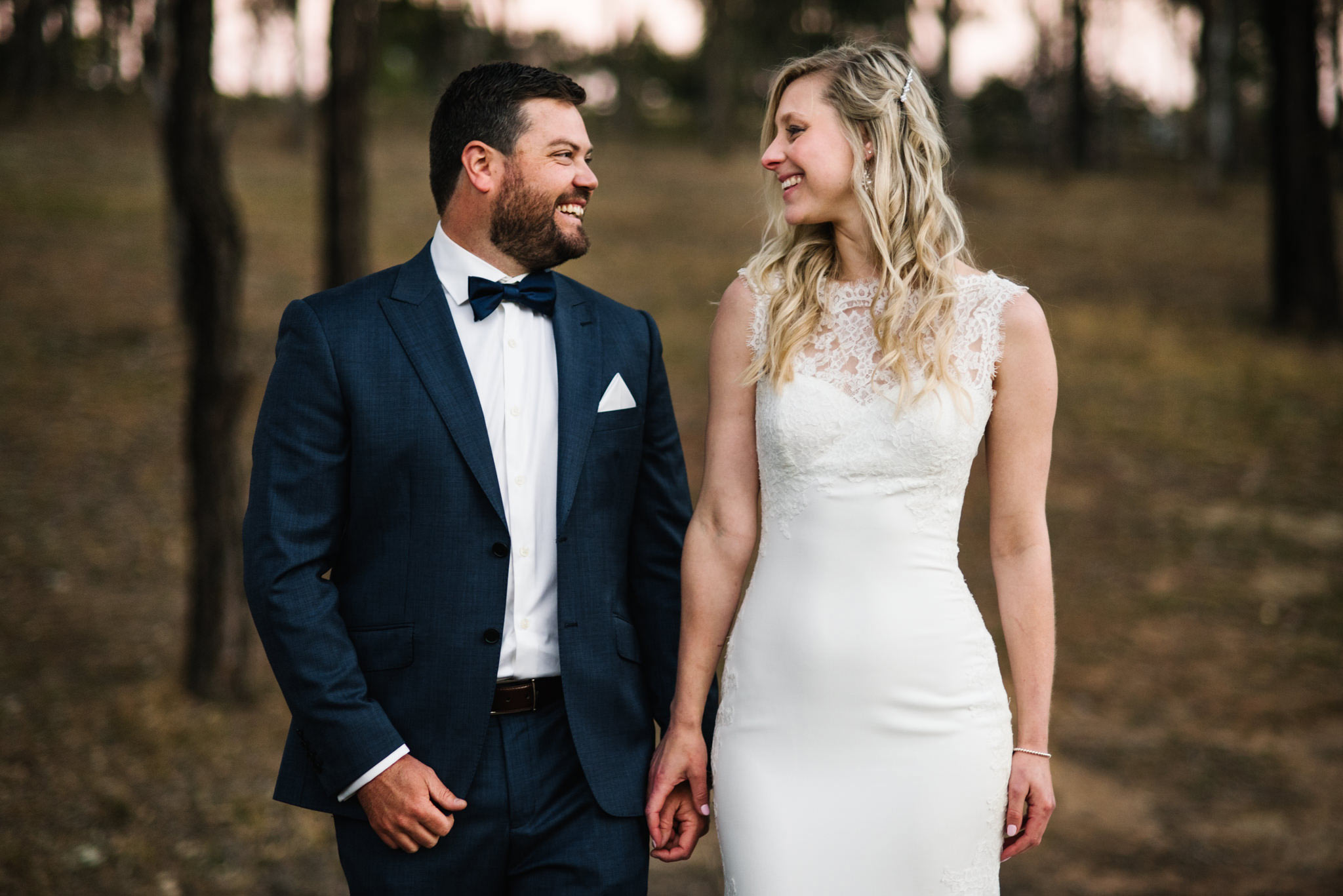 Happy newlyweds looking at each other with trees behind