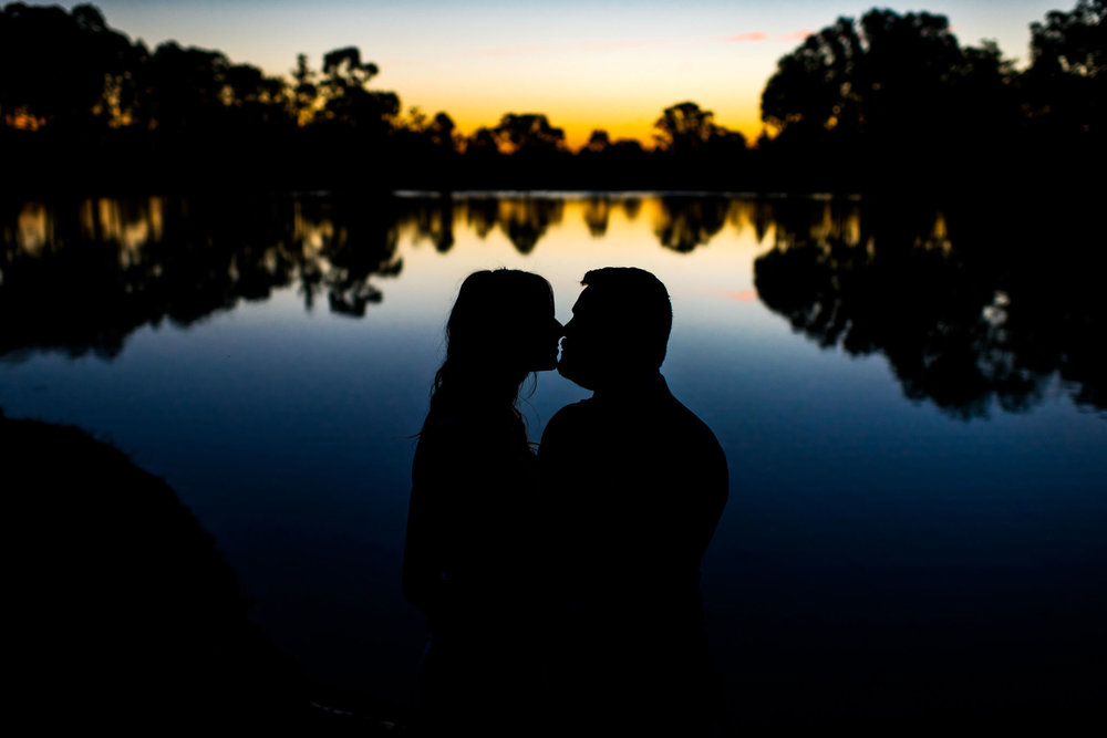 Silhouette of bride and groom kissing in front of a lake at sunset