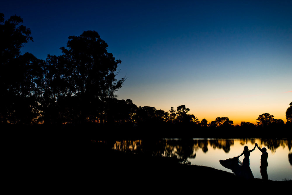 Bride and groom dance in front of lake during sunset