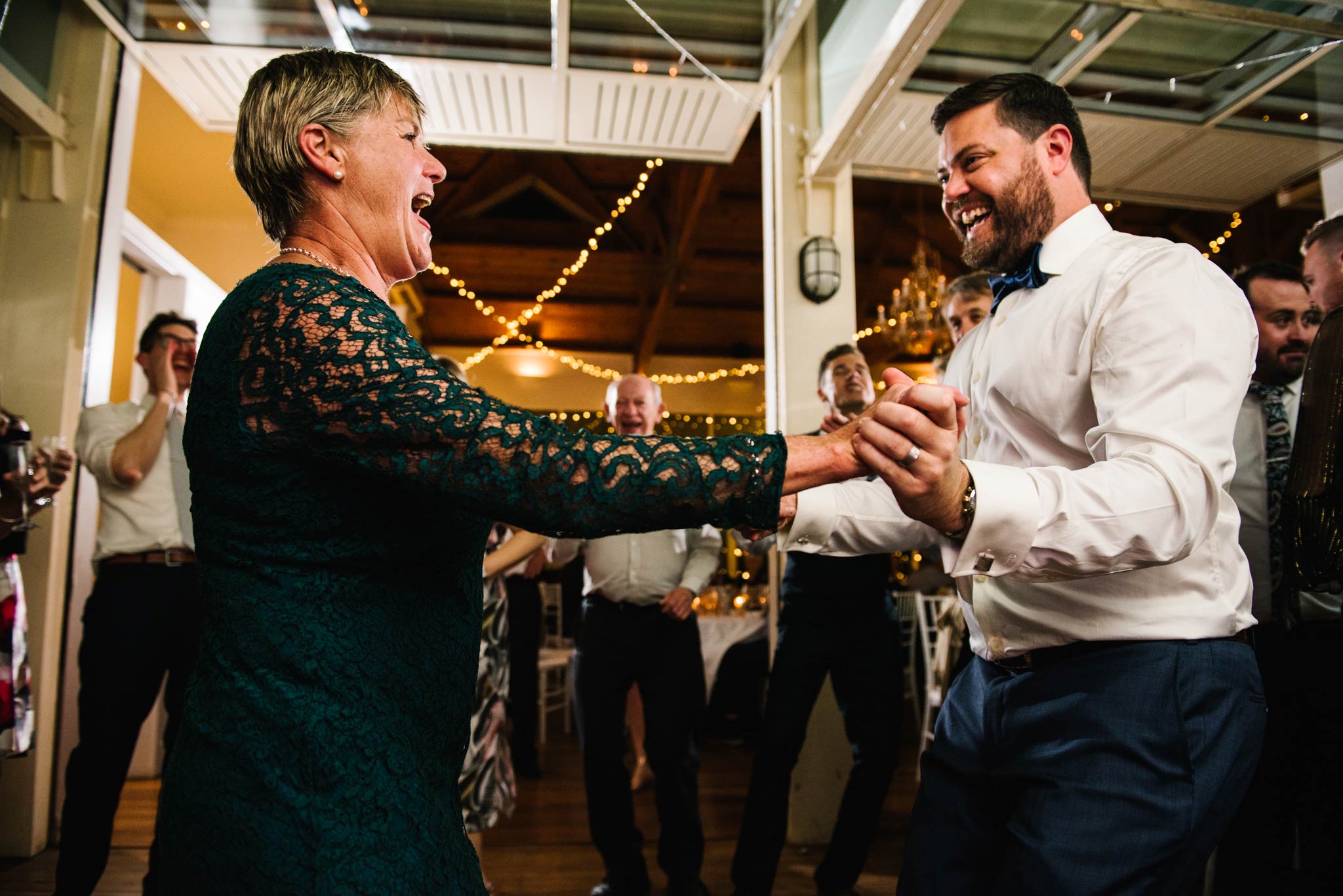 Mother and groom dancing together with guests watching in the background