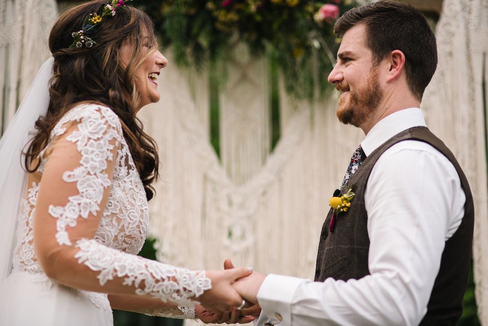 Bride and groom smile during ceremony, holding hands