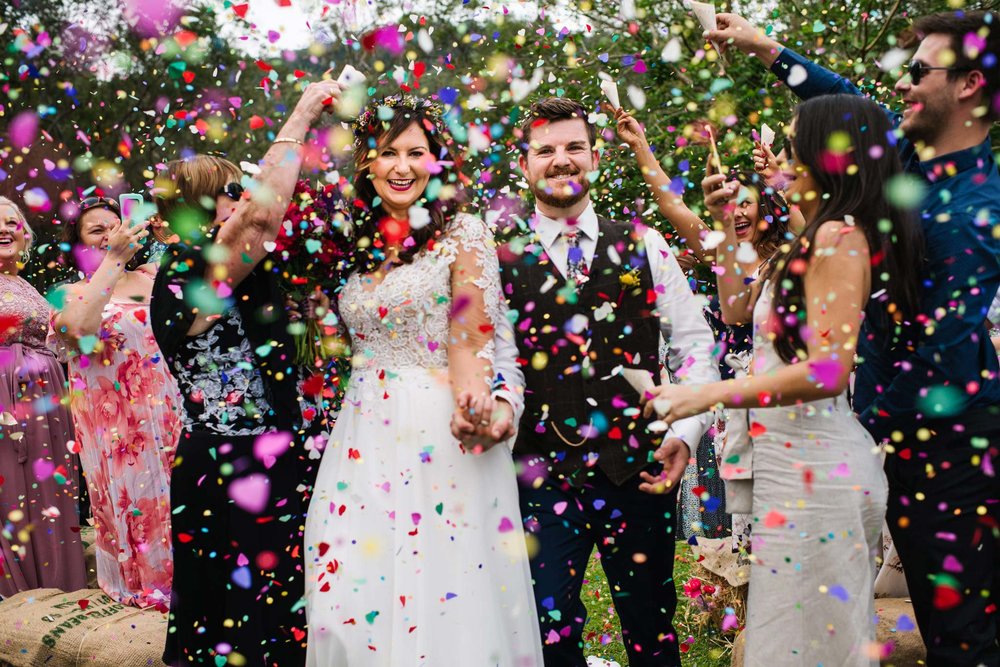 Rainbow confetti showers over smiling bride and groom