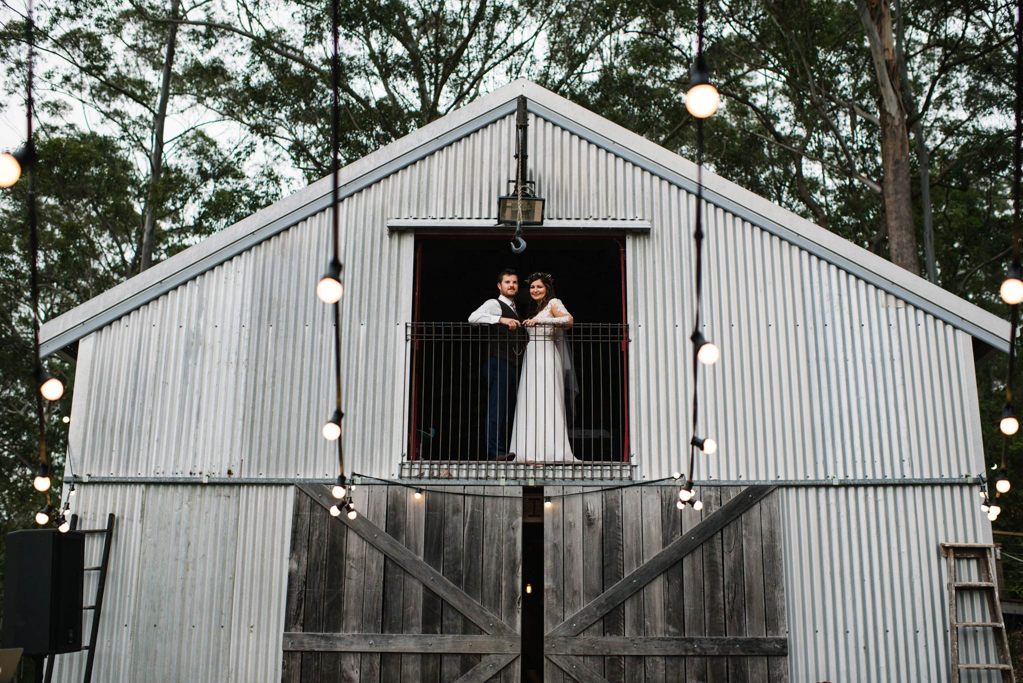 Bride and groom posing in the upper window of a barn