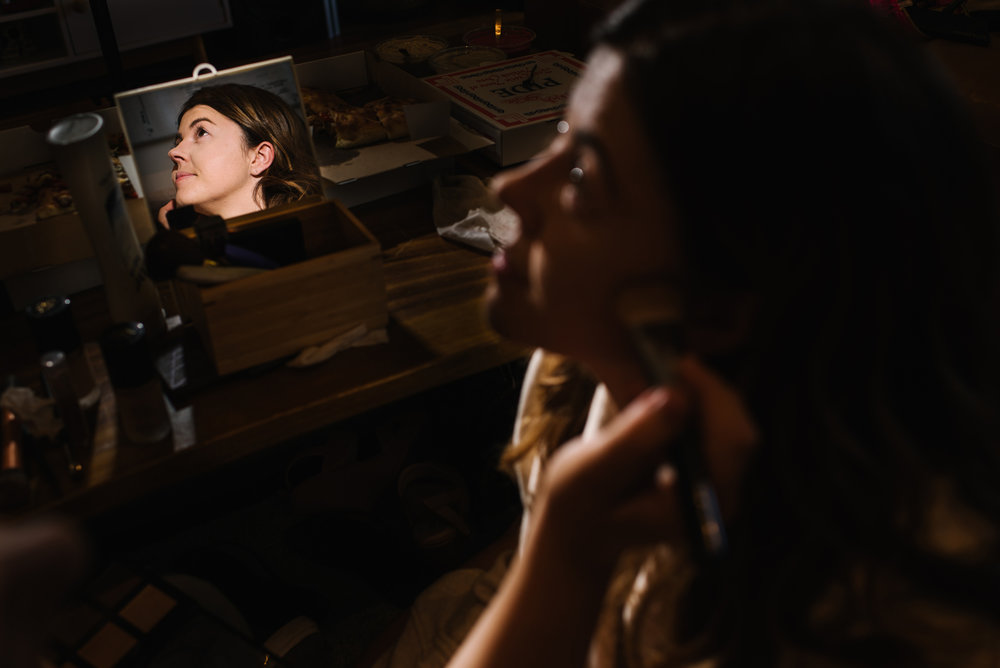 Reflection of bride in a small makeup mirror with makeup artist in background