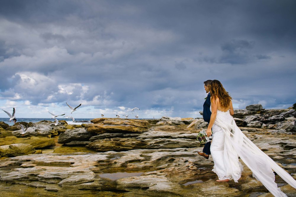 Newlyweds walk along rocky outcrops at Little Bay