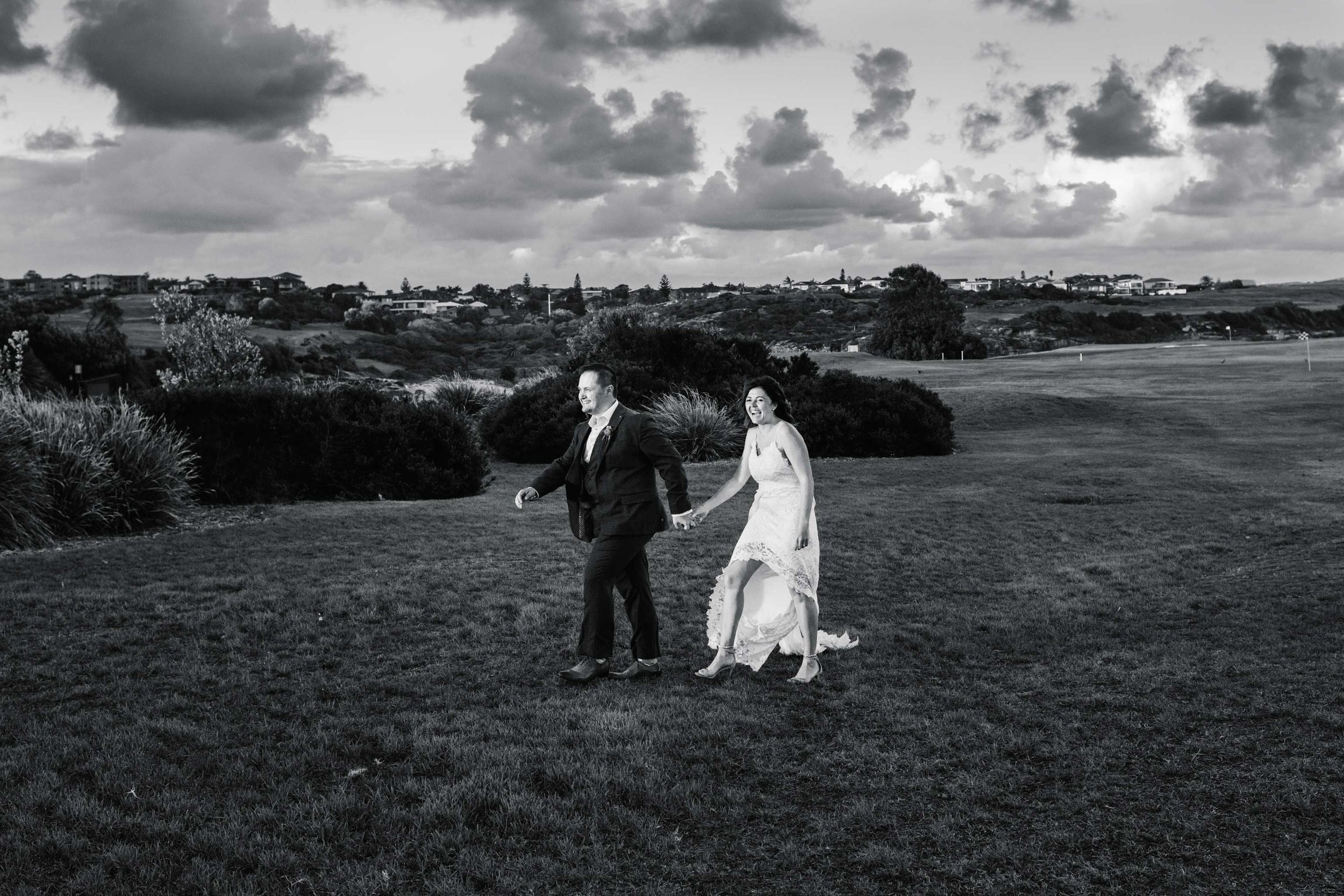 Bride and groom walking across lawn at Coast Golf Club Little Bay