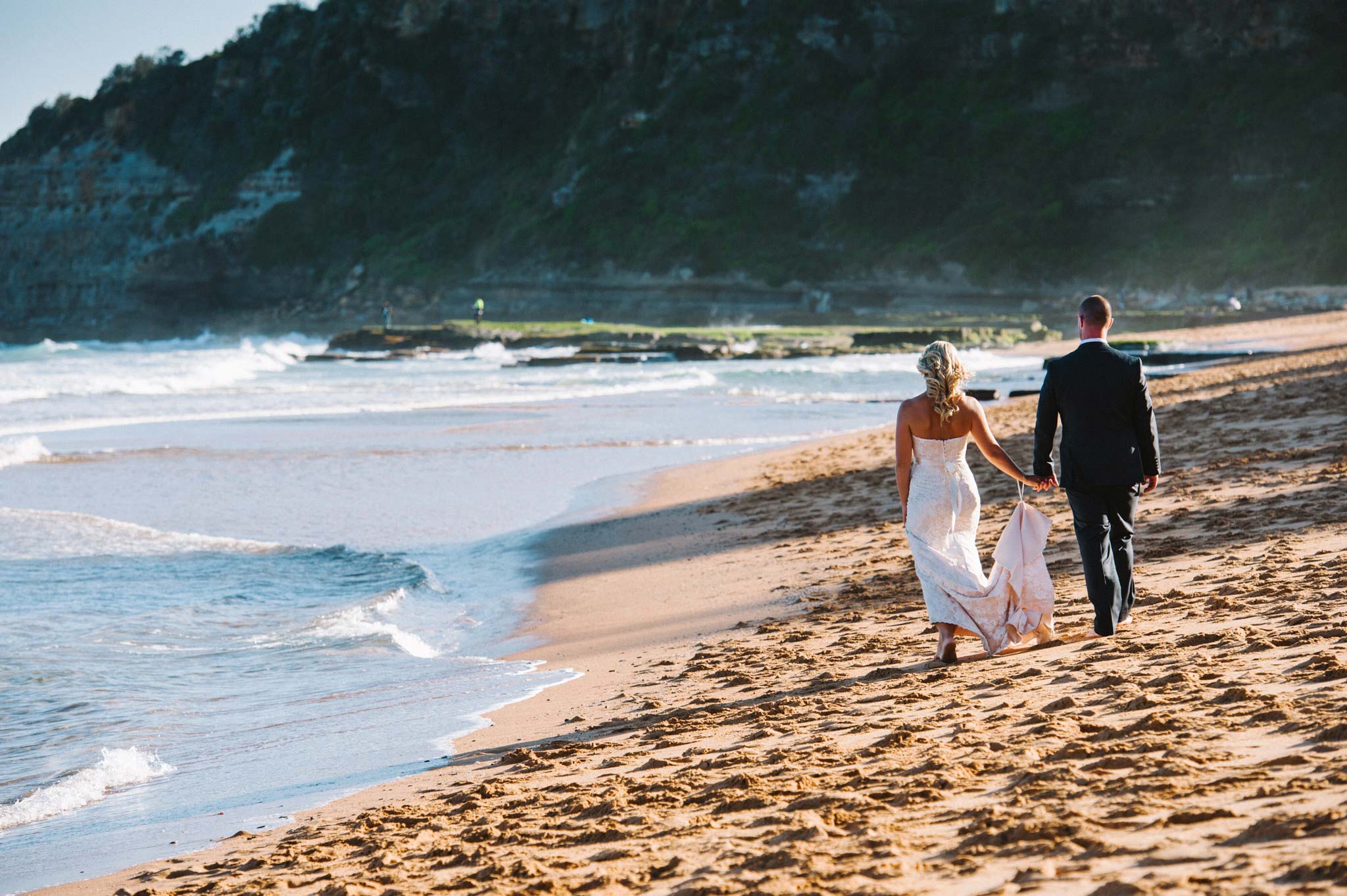 Newlyweds walking along beach at Turimetta