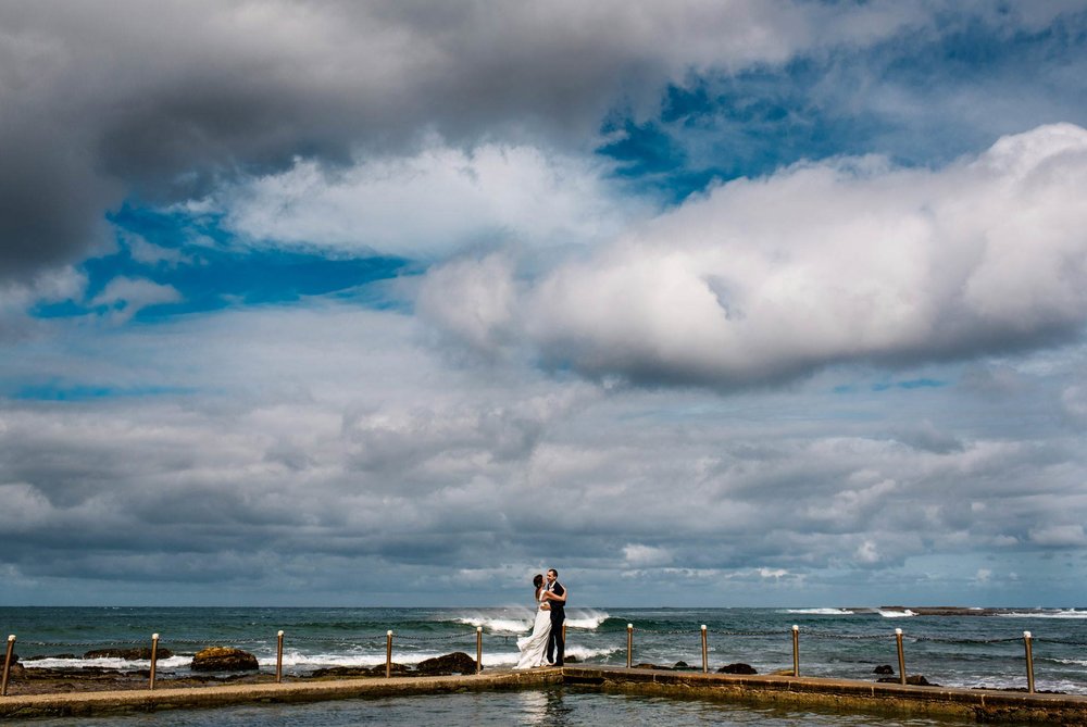 Newlyweds under expansive sky at Mona Vale beach