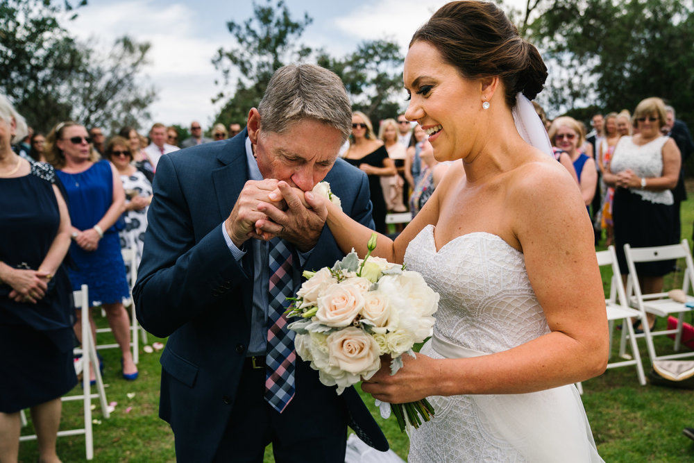 Father kissing bride's hand at the end of the aisle