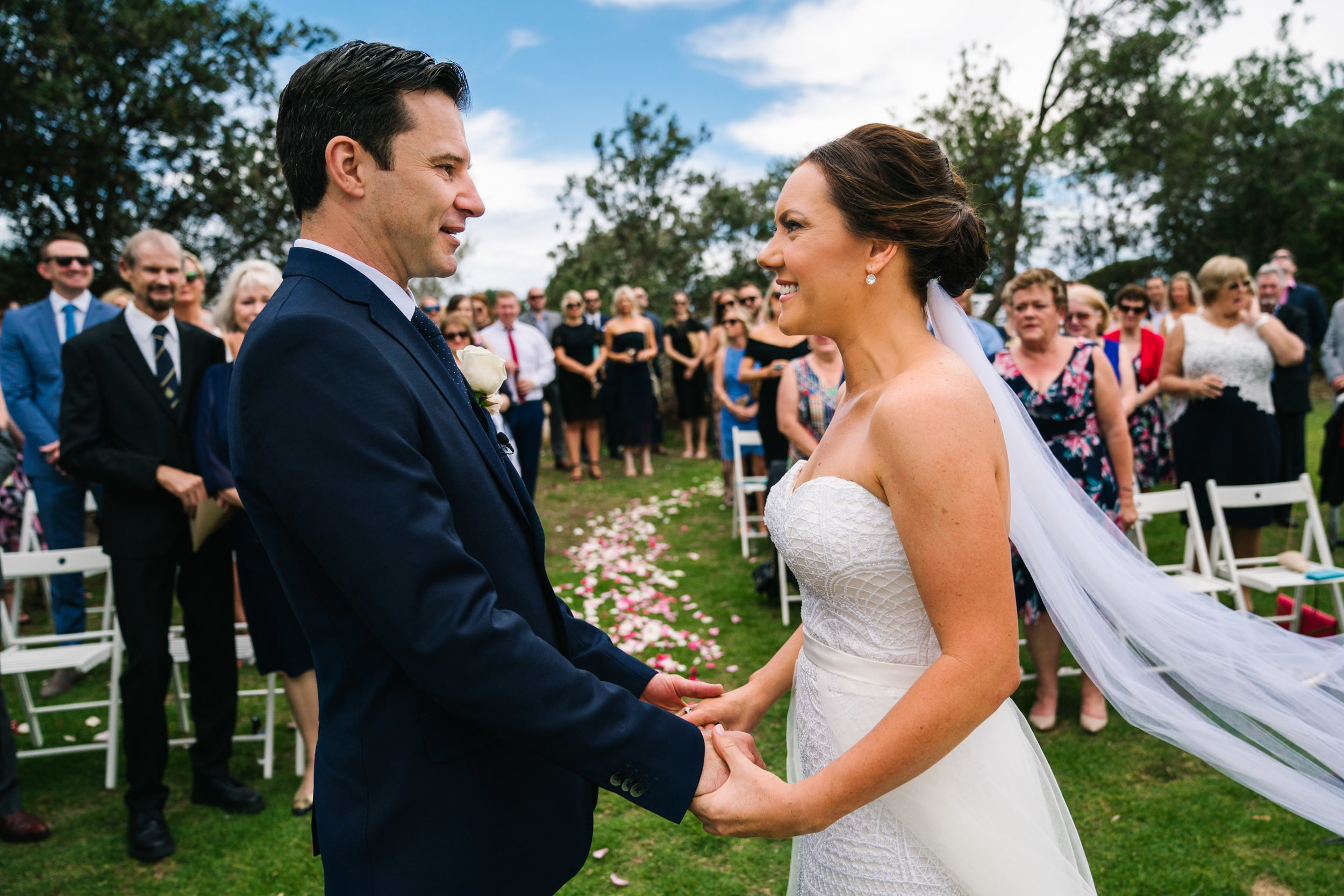 Bride and groom smiling while guests look on at their Shelly Beach wedding
