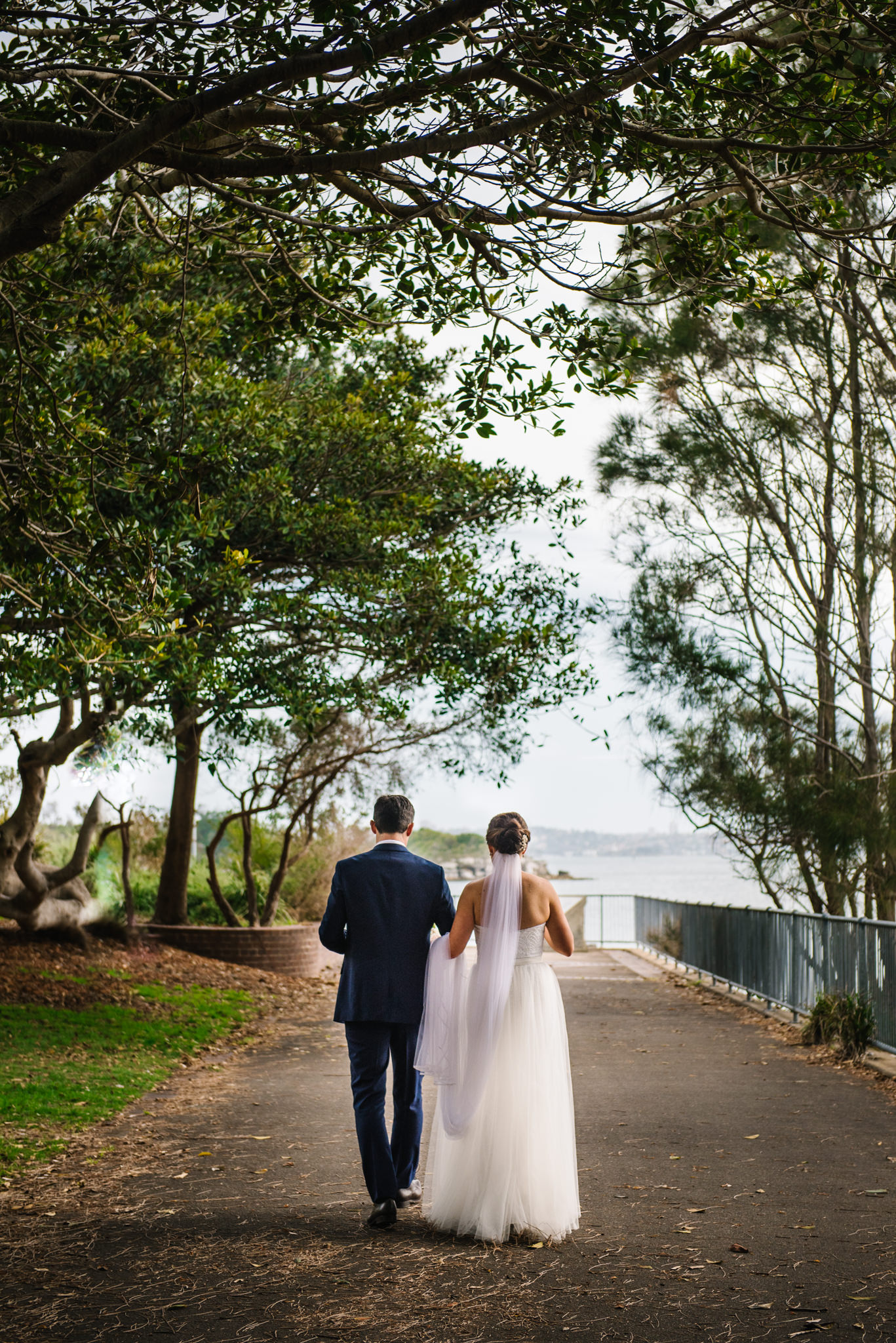 Bride and groom walking down aisle of trees at Little Manly