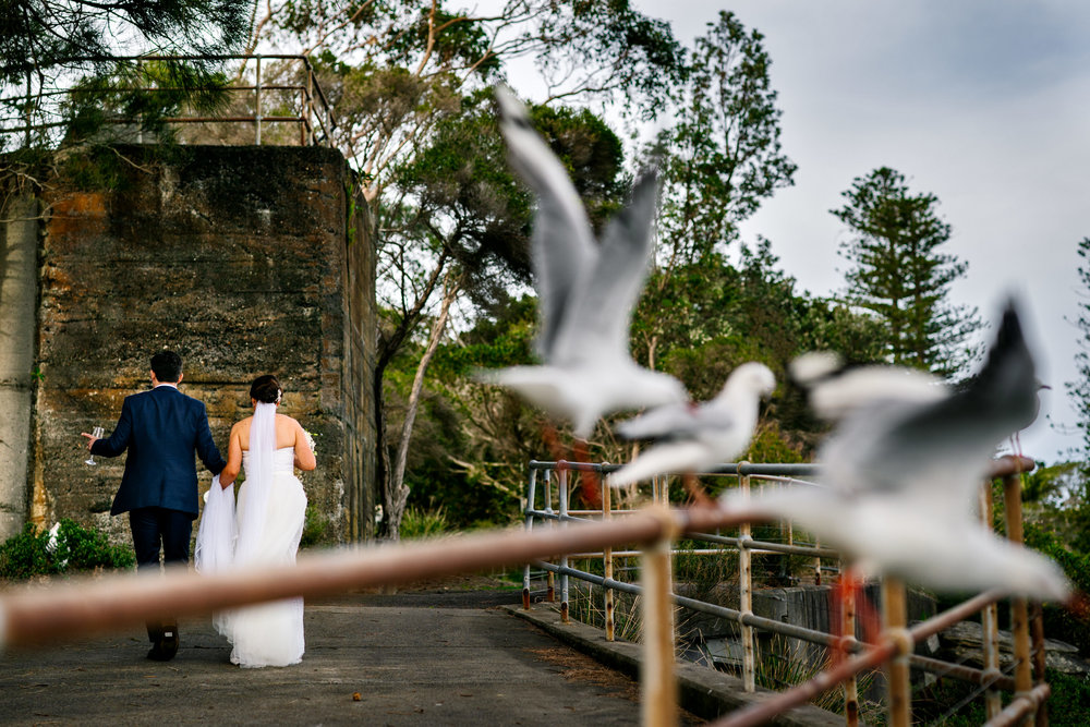 Bride and groom walking with birds flying in the foreground
