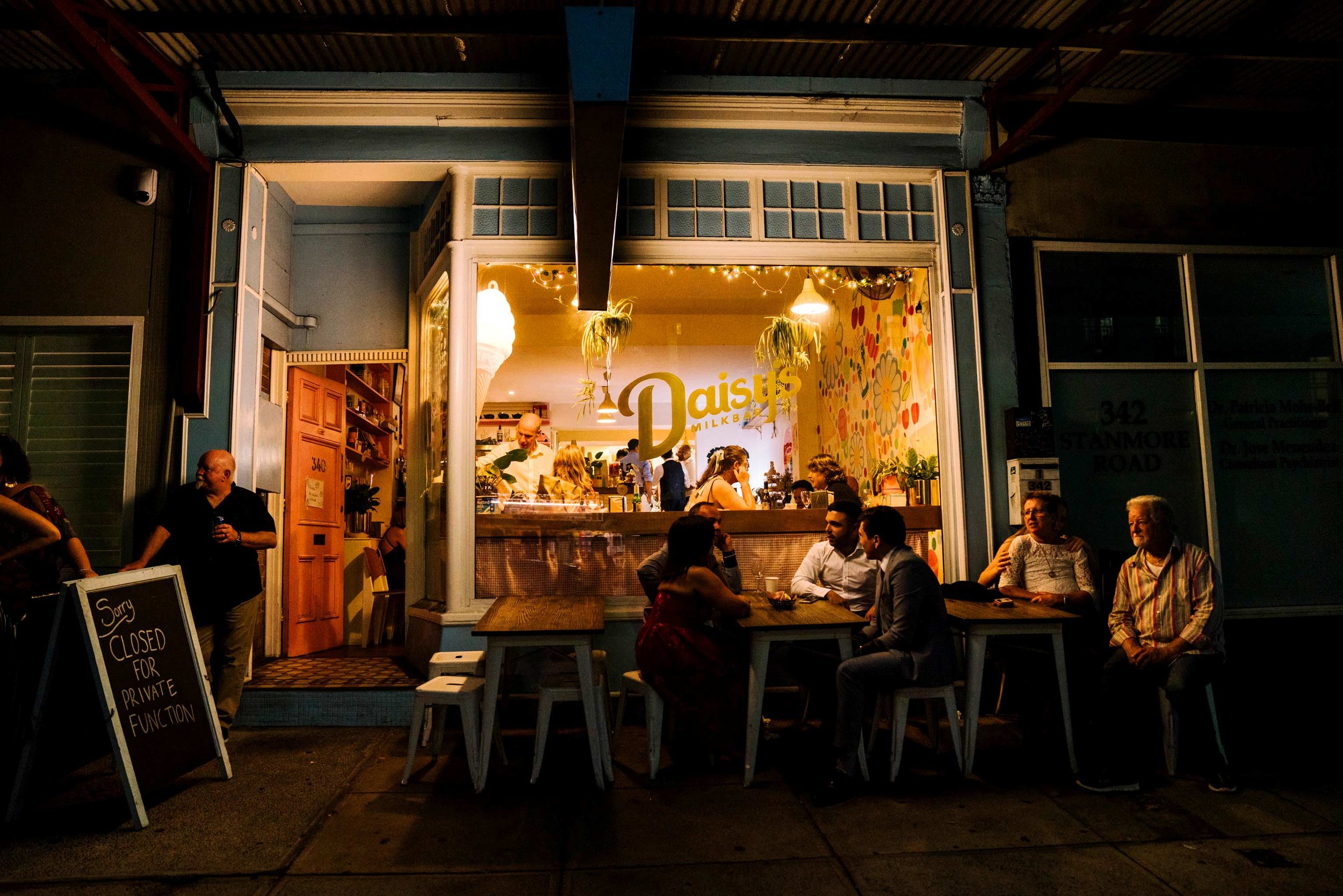 View of Daisy's Milk bar at night with wedding guests out front