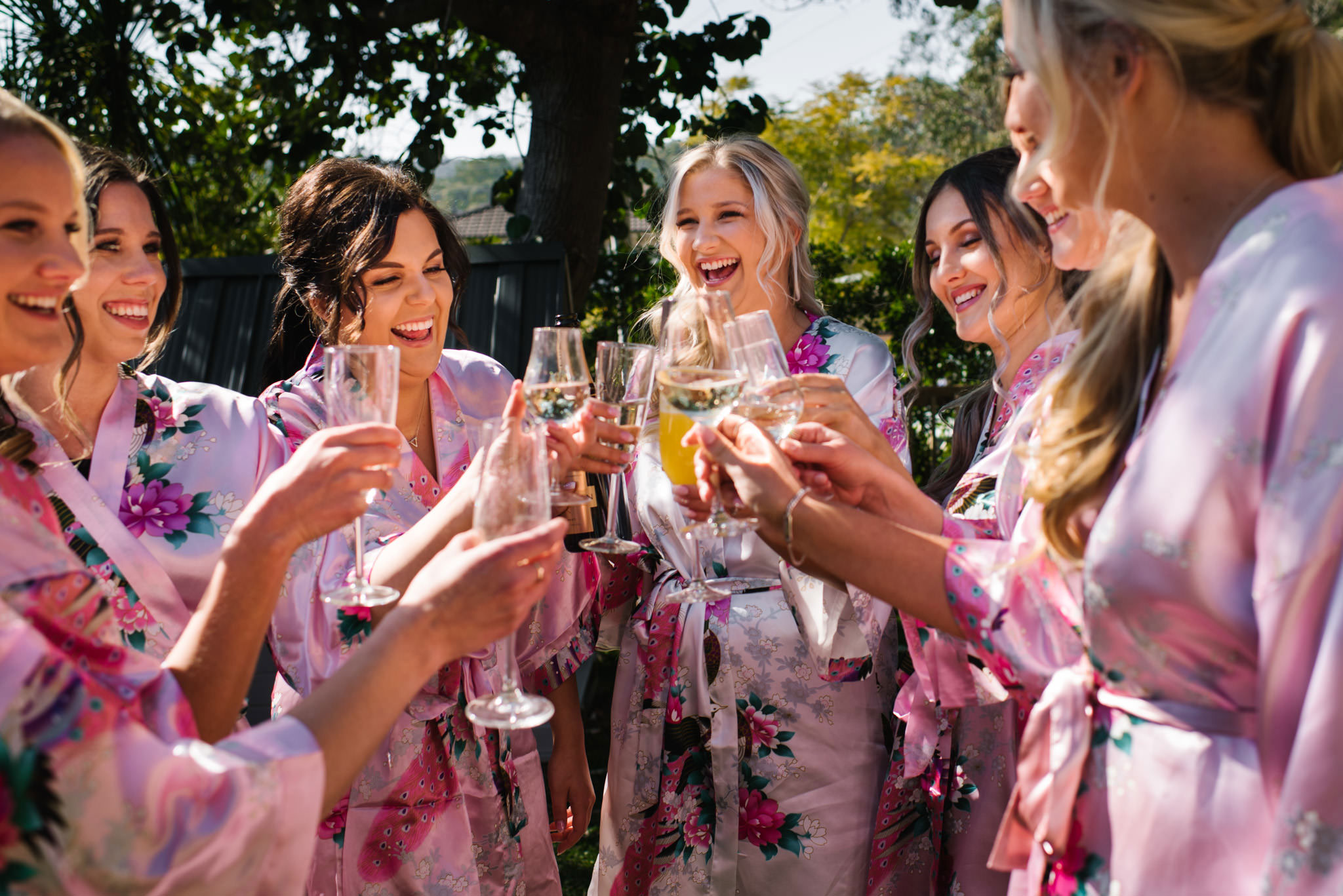 Bride and bridesmaids in pink floral dressing gowns cheers with champagne