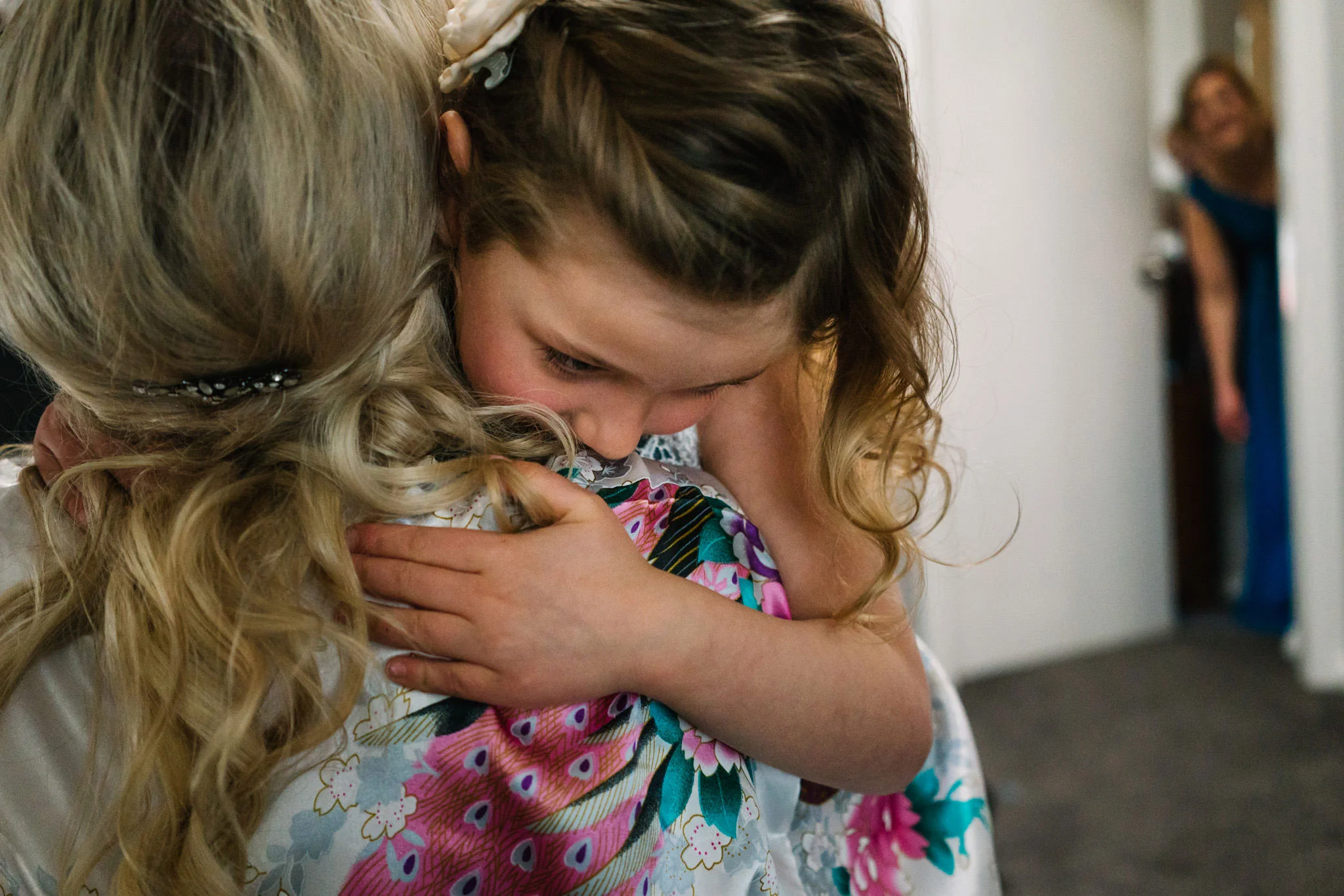 Flowergirl and bride hugging with bridesmaid watching in the background