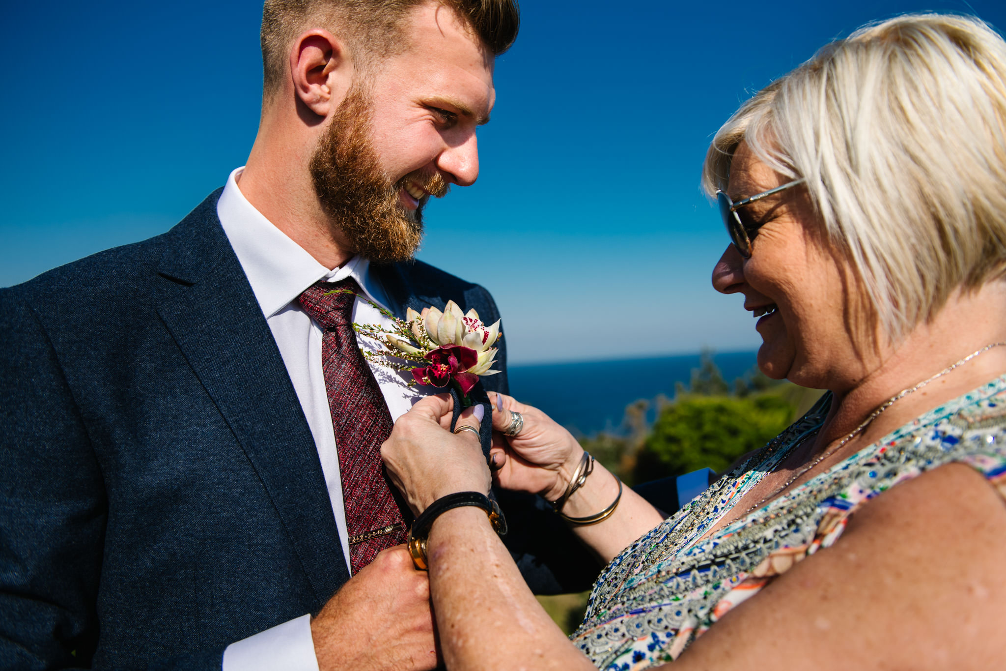 Groom's mother attaching his buttonhole with the beach in the background