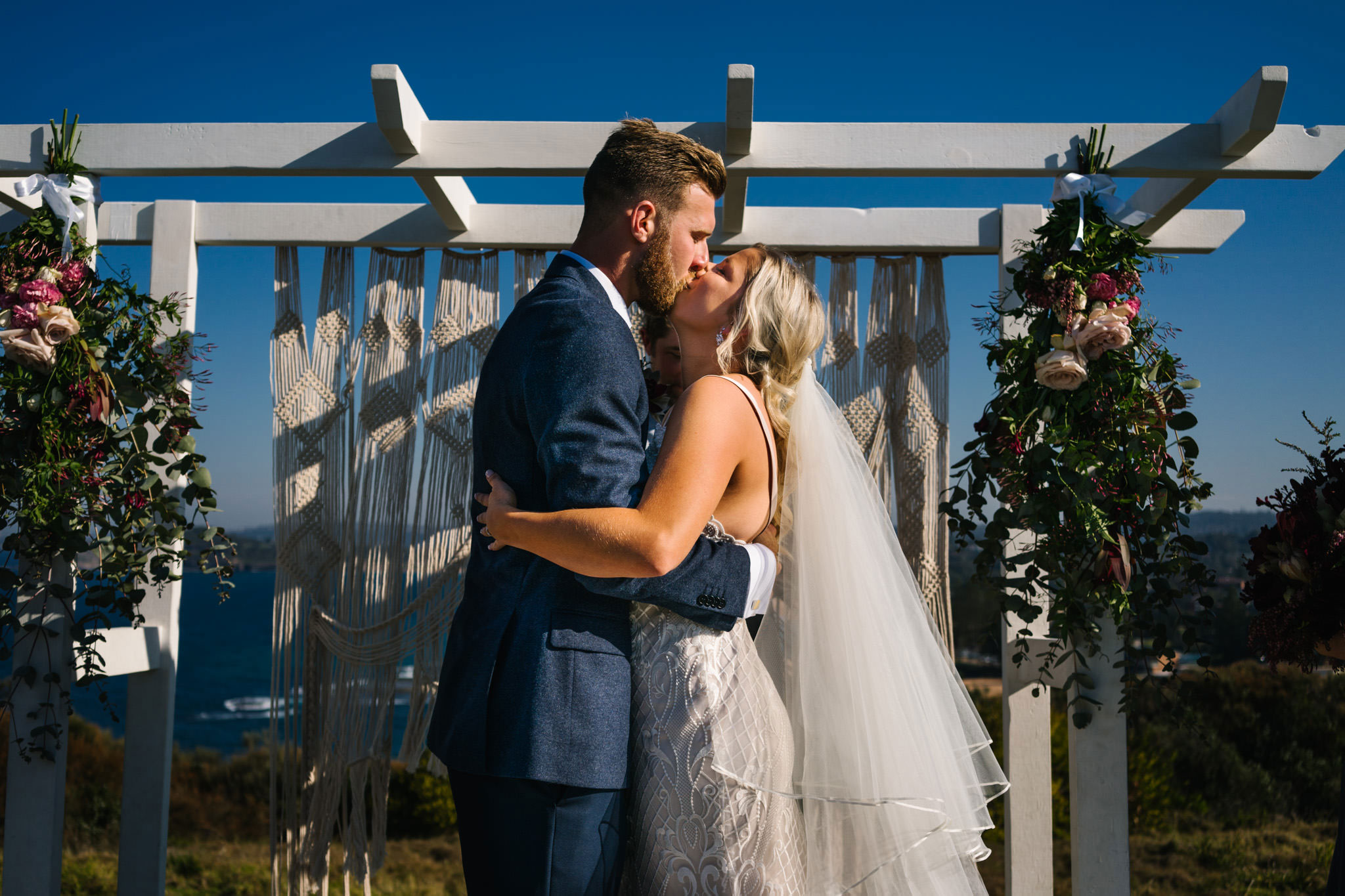 Newlyweds first kiss under boho wedding altar at outdoor headland ceremony
