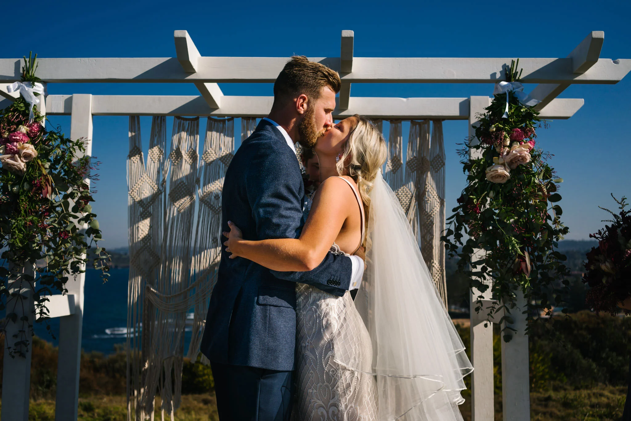 Newlyweds first kiss under boho wedding altar at outdoor headland ceremony