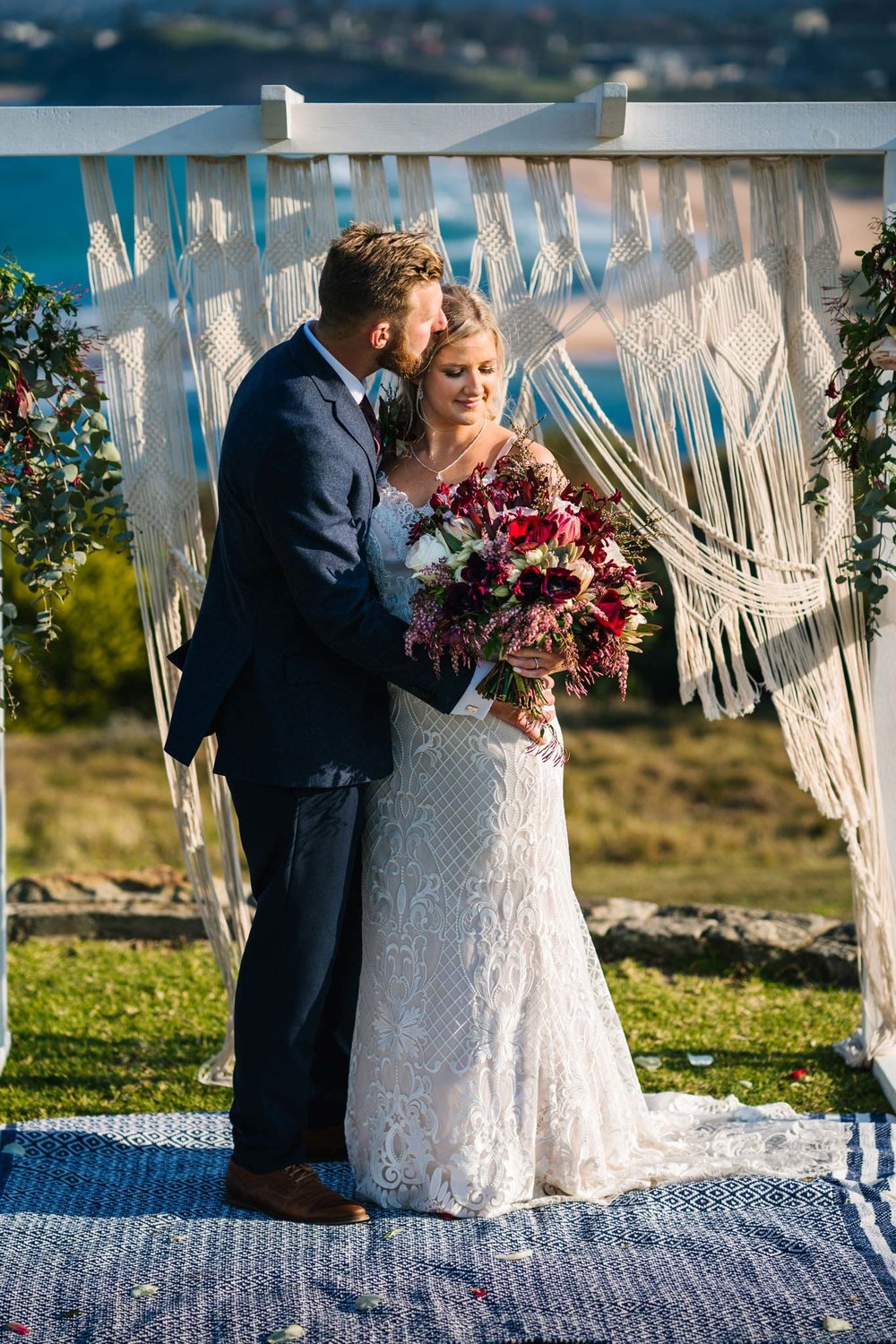 Newlyweds pose in front of their macrame boho wedding altar on Mona Vale headland